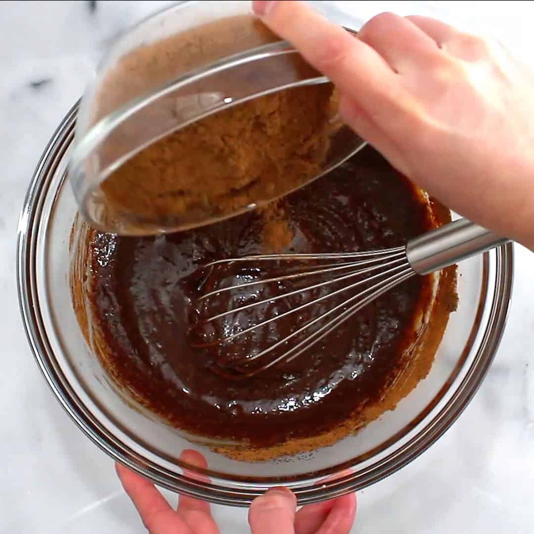 hand pouring cocoa powder into wet ingredient mixture for vegan brownie batter