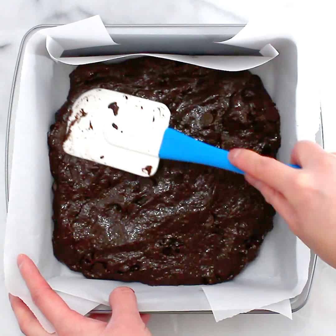 Smoothing vegan brownie batter into an even layer in parchment paper lined baking pan