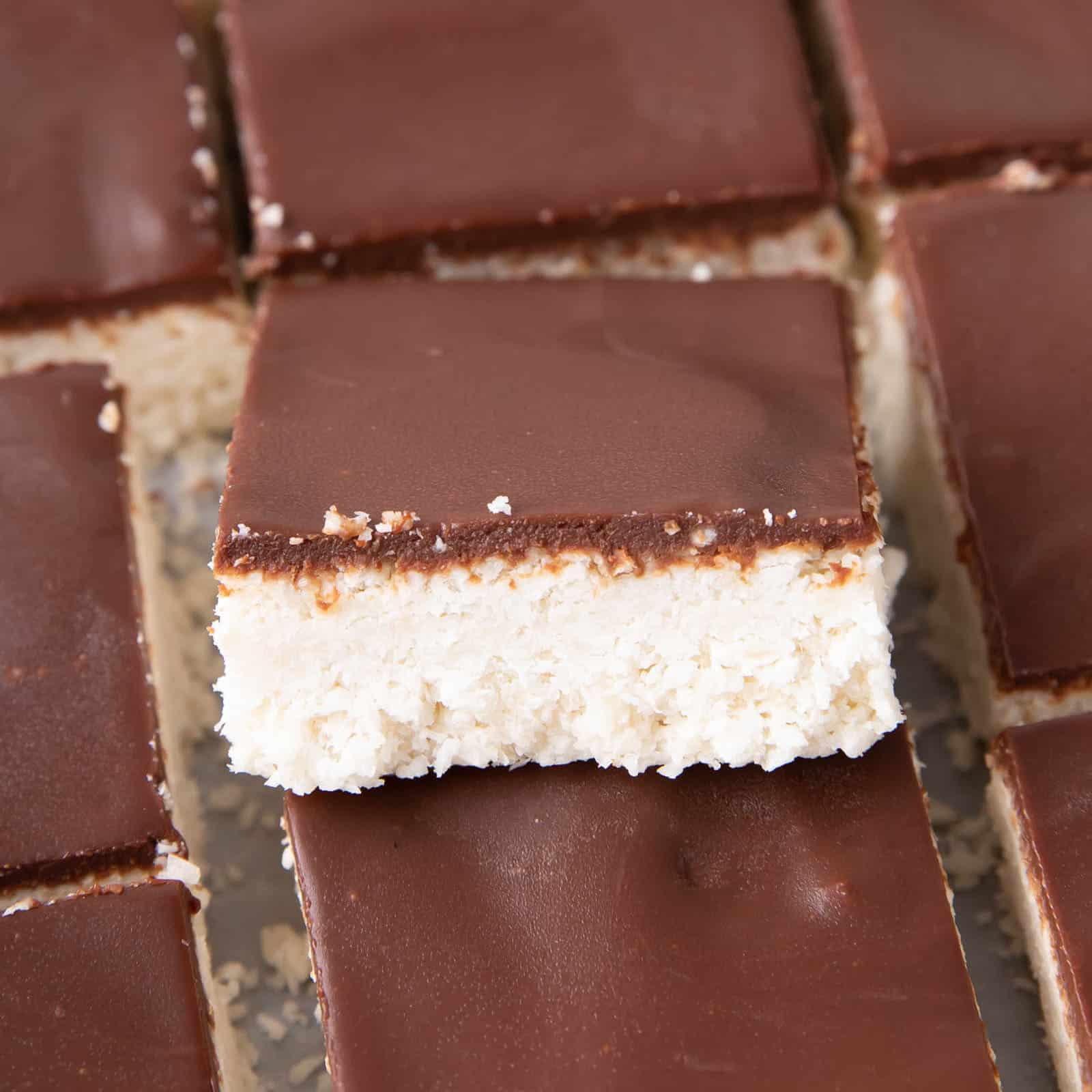 Overhead picture of vegan coconut bars with chocolate topping, one square perched on top of the rest at an angle
