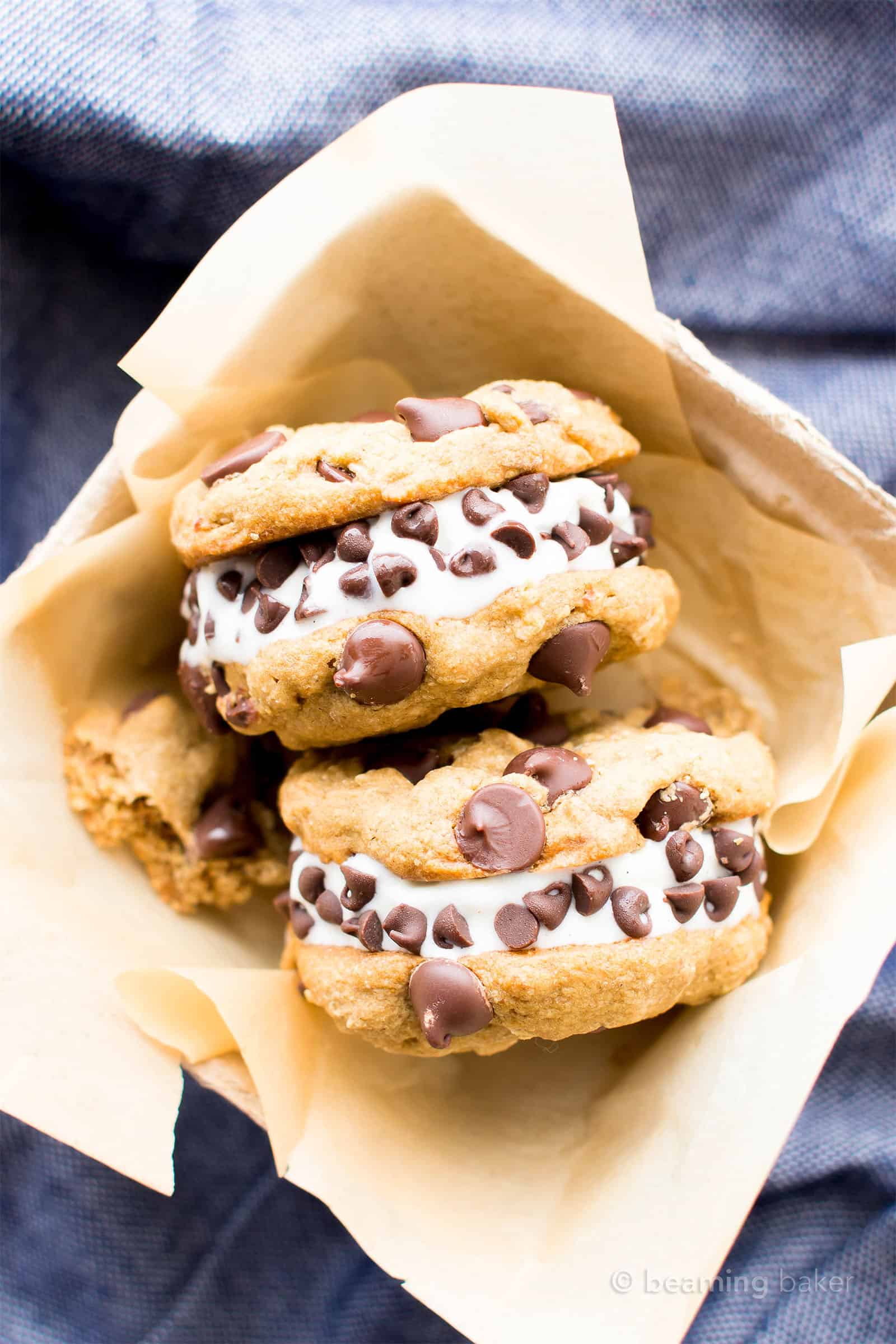 Two vegan gluten free ice cream sandwiches with cookie tops and chocolate chips in parchment paper container