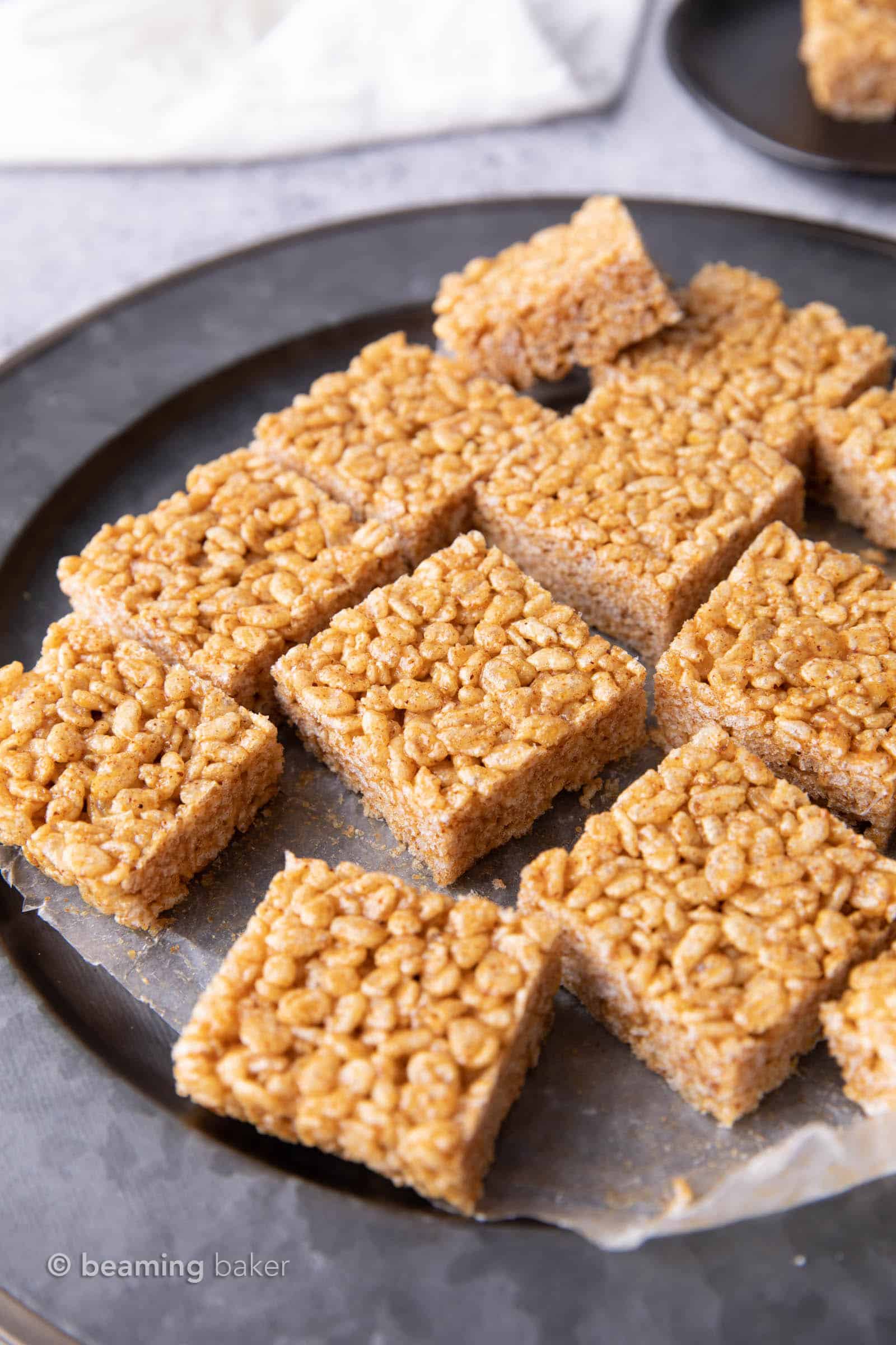 many healthy rice crispy treats on a gray serving tray with a plate of treats in the background