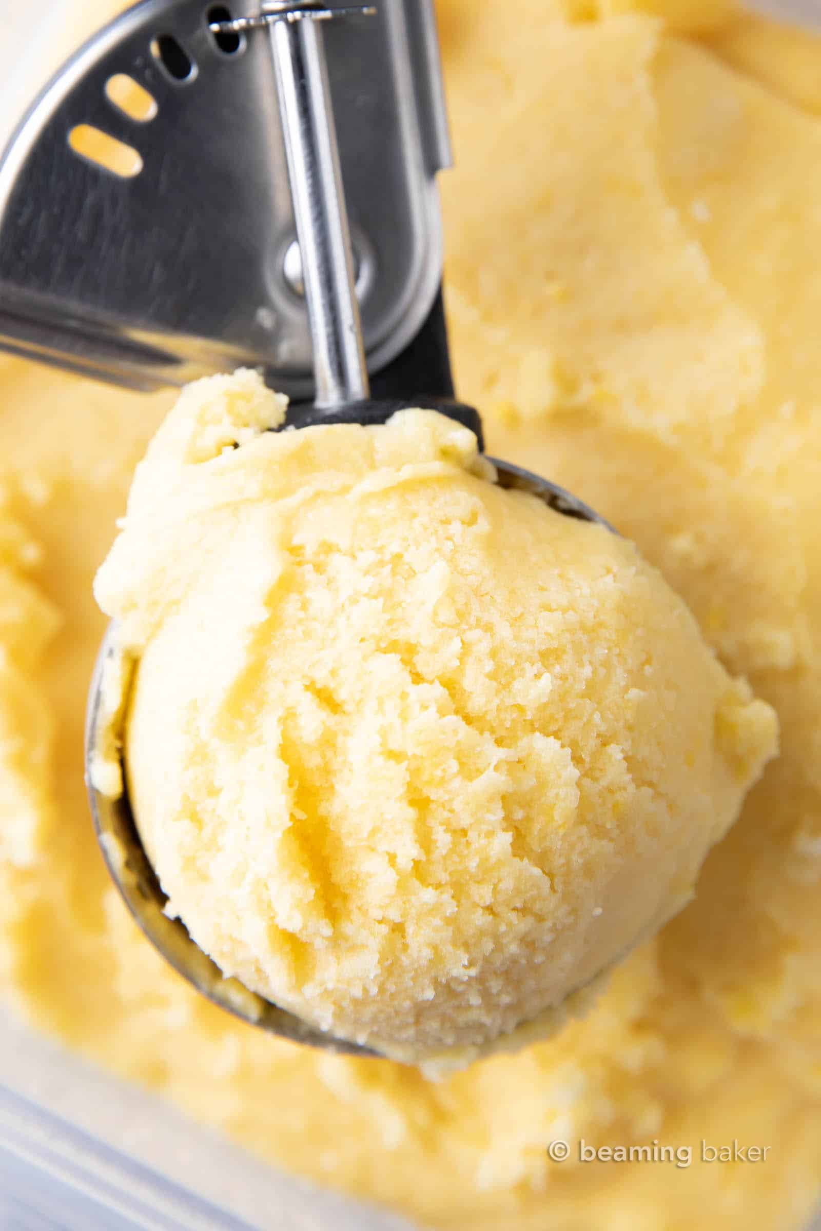 Scooping homemade mango ice cream out of the container.