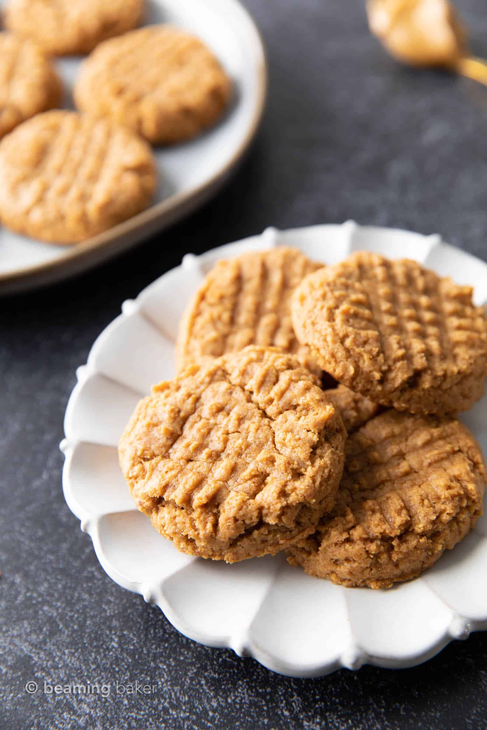 Four gluten free peanut butter cookies stacked and spread out on a white plate.