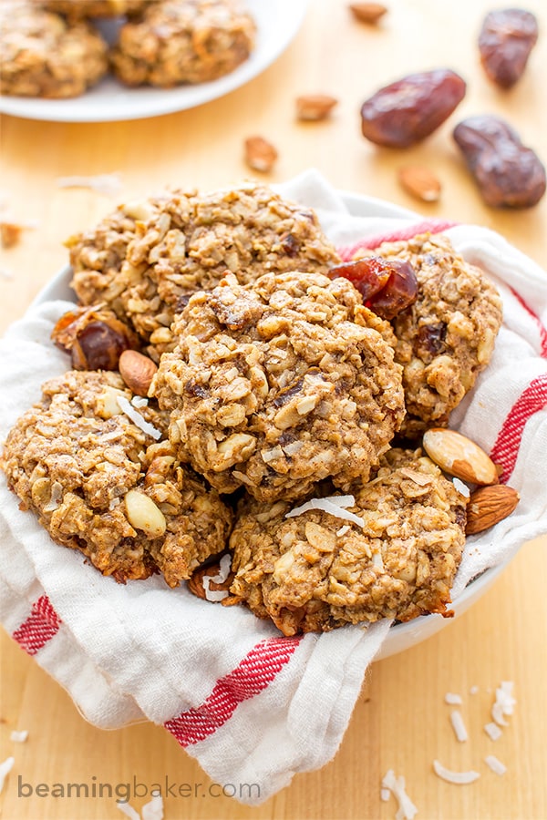 Basket of vegan gluten free breakfast cookies in a white and red stripe towel, with dates, almonds and coconut in the background