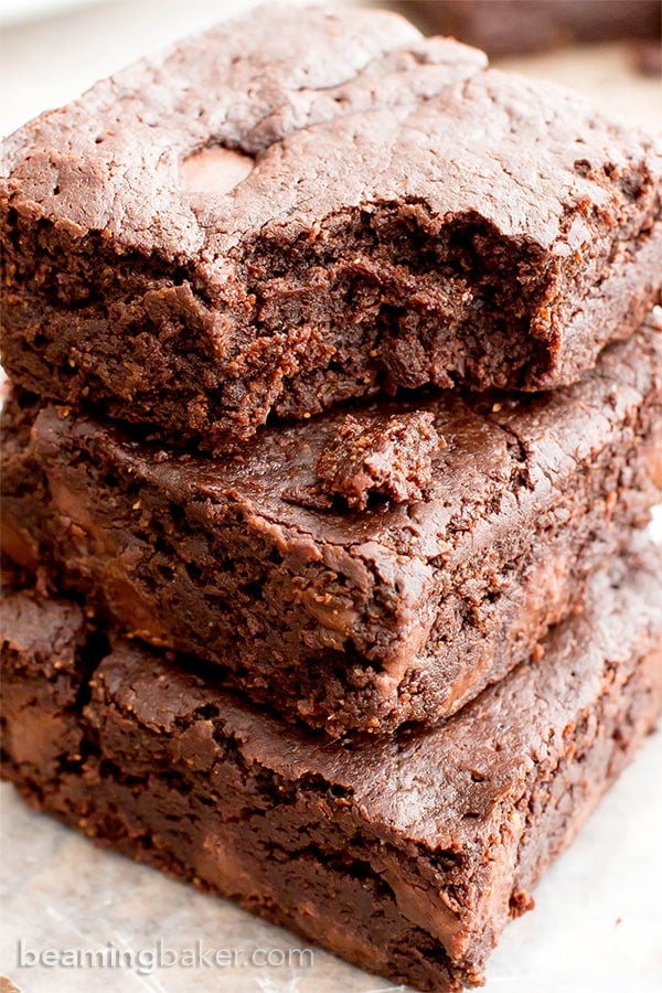 one vegan gf brownie bitten sitting atop two other brownies on wax paper