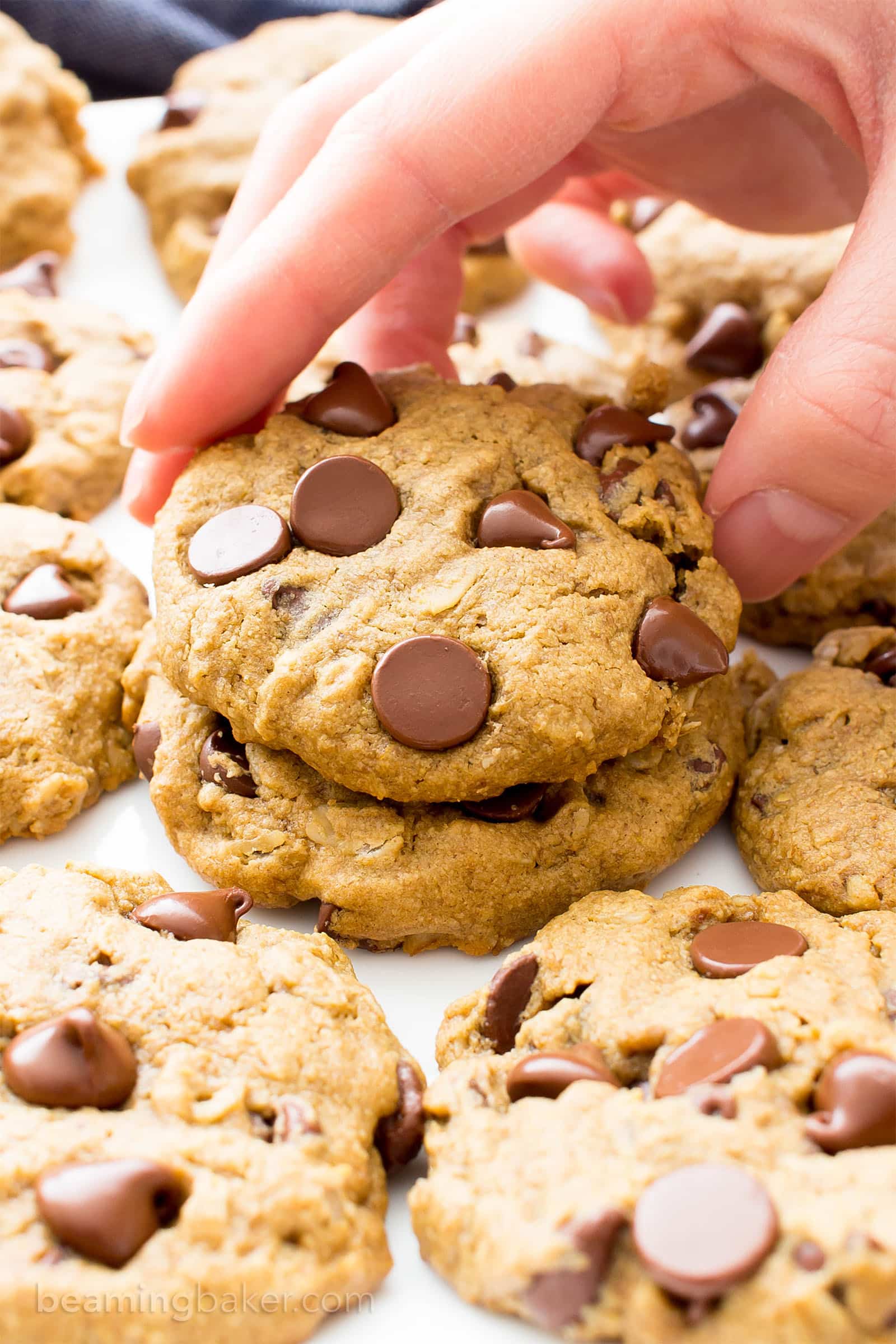 Hand picking up an oat flour cookie from plate with several more cookies on it