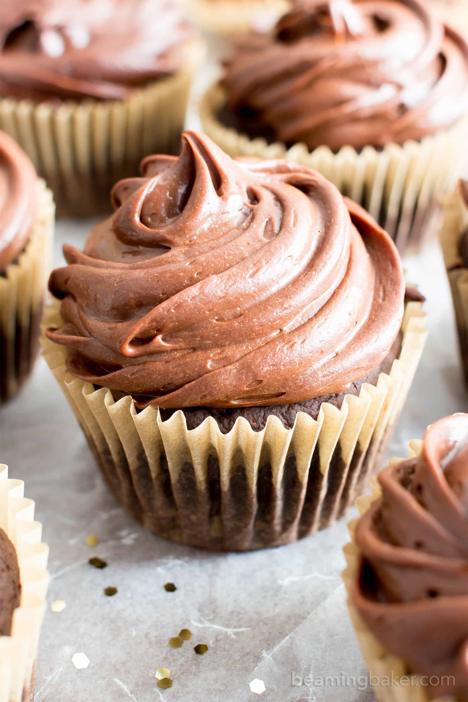 Vegan gluten free chocolate cupcakes with chocolate frosting on parchment paper