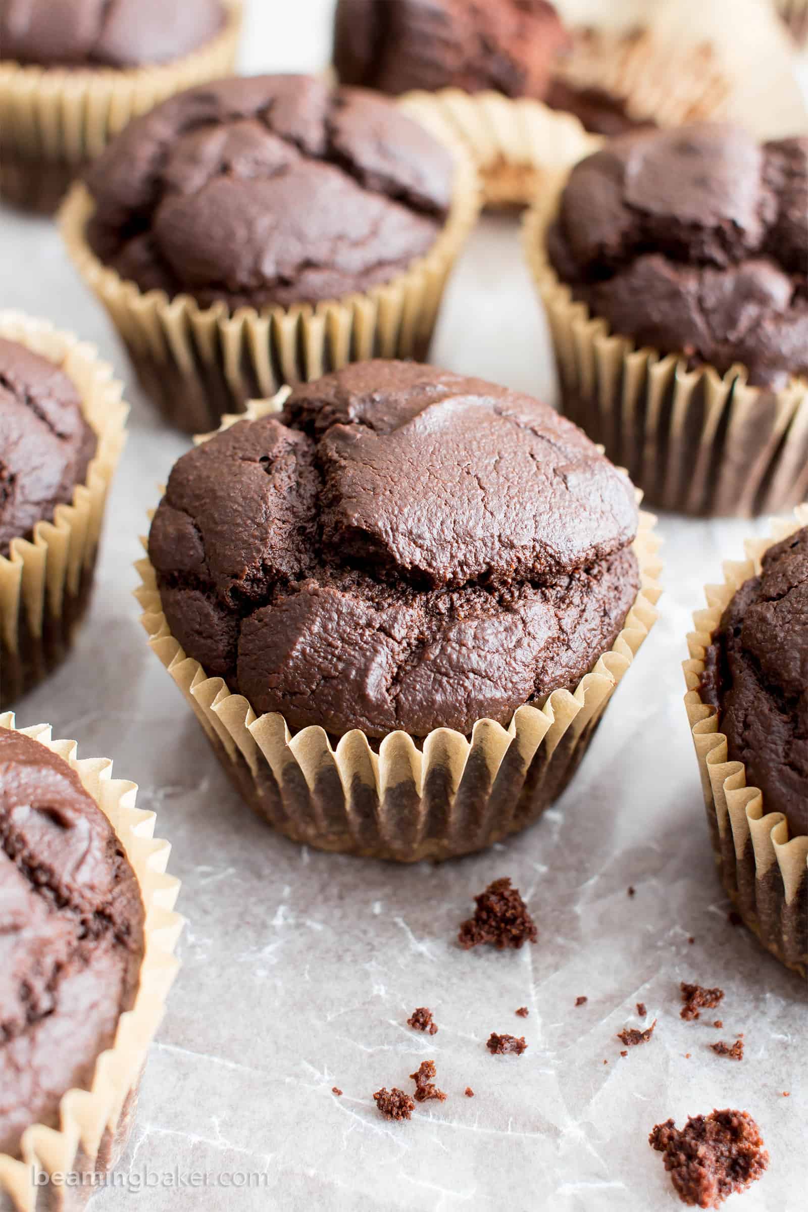 Several vegan gluten free chocolate muffins on parchment paper with crumbs in the lower right corner