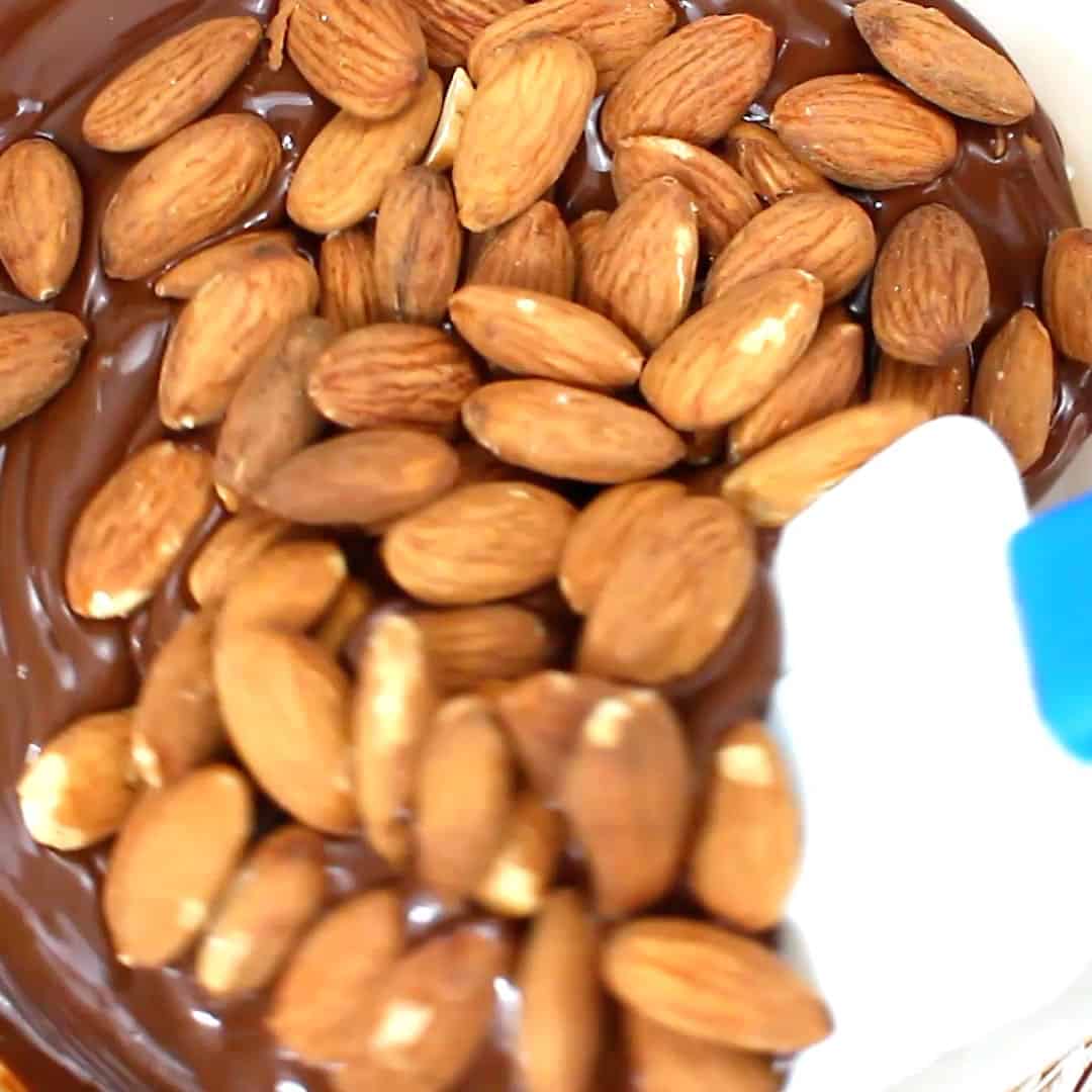 spatula folding almonds into melted chocolate for vegan almond bark