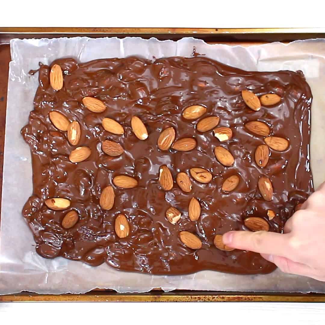finger pressing almonds into spread out melted chocolate almond bark
