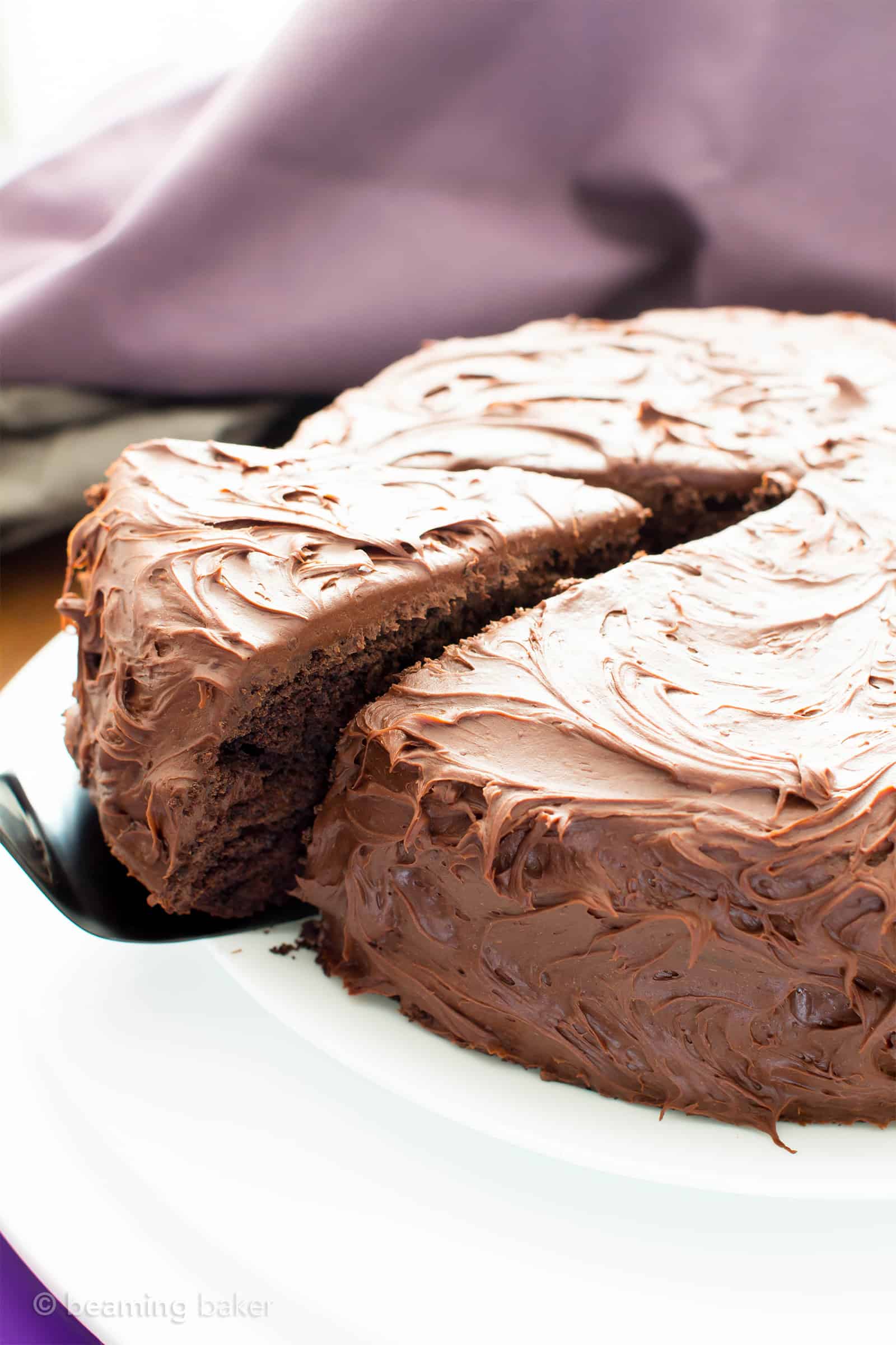 Slice of gluten free dairy free chocolate cake being pulled out of the remainder of the cake.