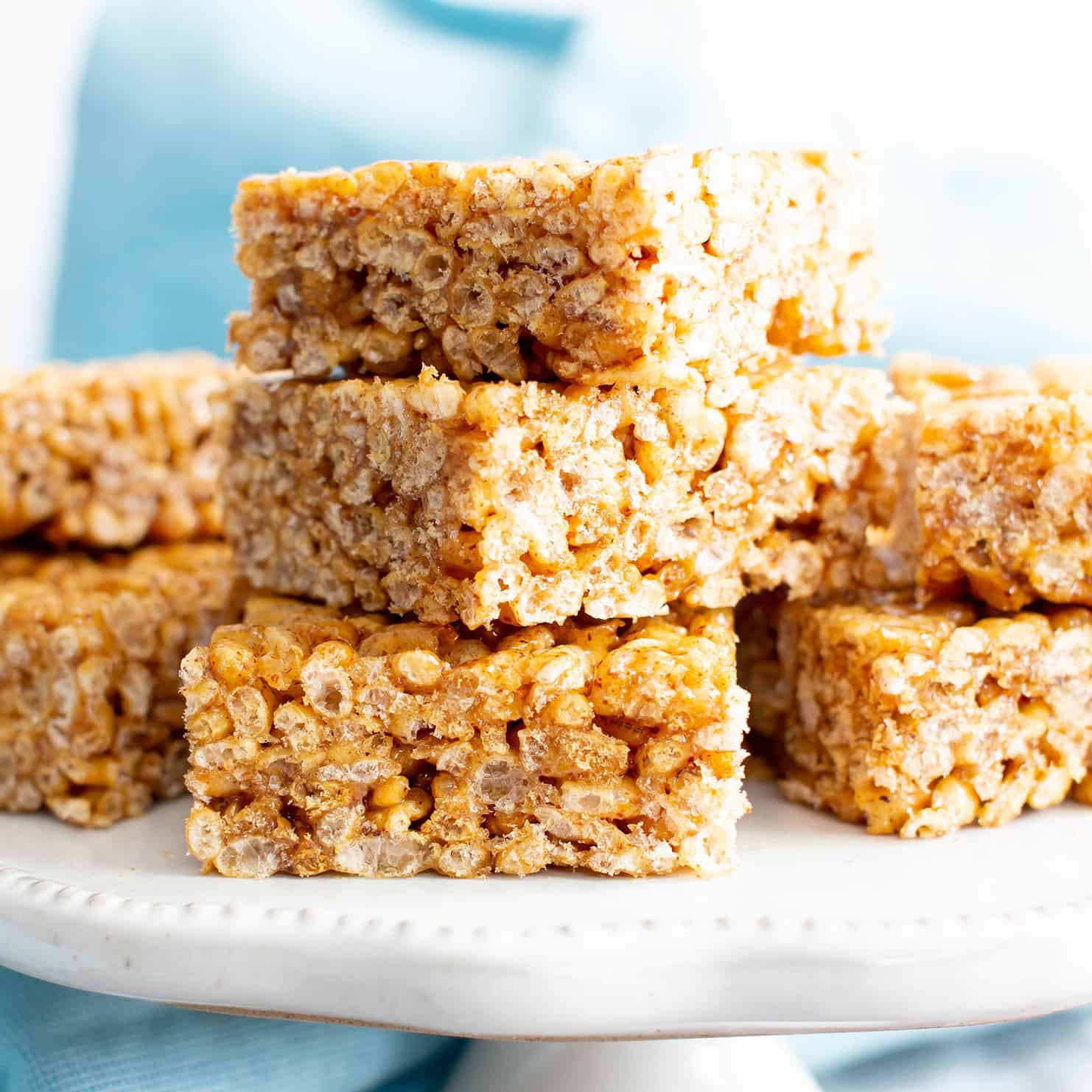Squares of vegan rice crispy treats on a white stand with a blue cloth in the background