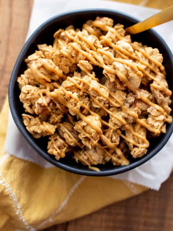 this peanut butter granola recipe in a black bowl with peanut butter drizzled on top