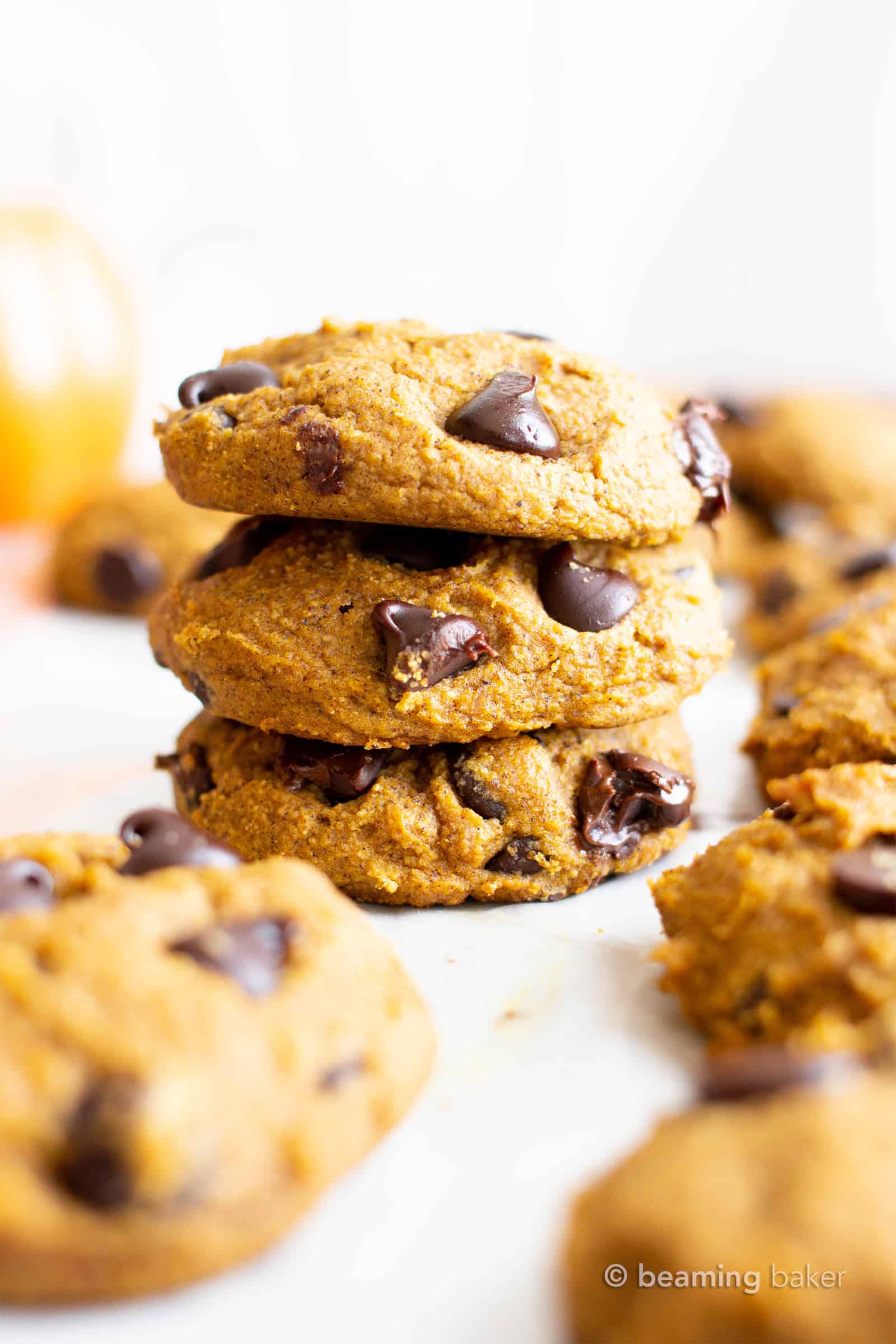 Stack of three vegan gluten free pumpkin cookies with chocolate chips, and more cookies around it in the background