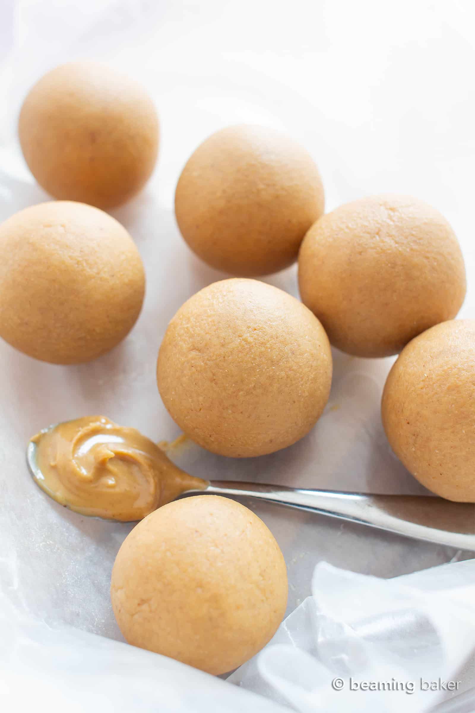 Keto energy balls on wax paper with a silver spoon of peanut butter nearby.