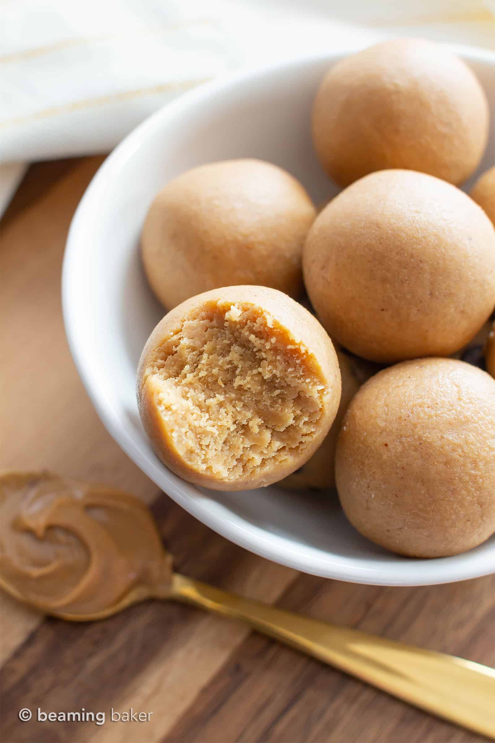 Bowl of keto balls sitting on the kitchen counter with a gold spoon of peanut butter beneath it.