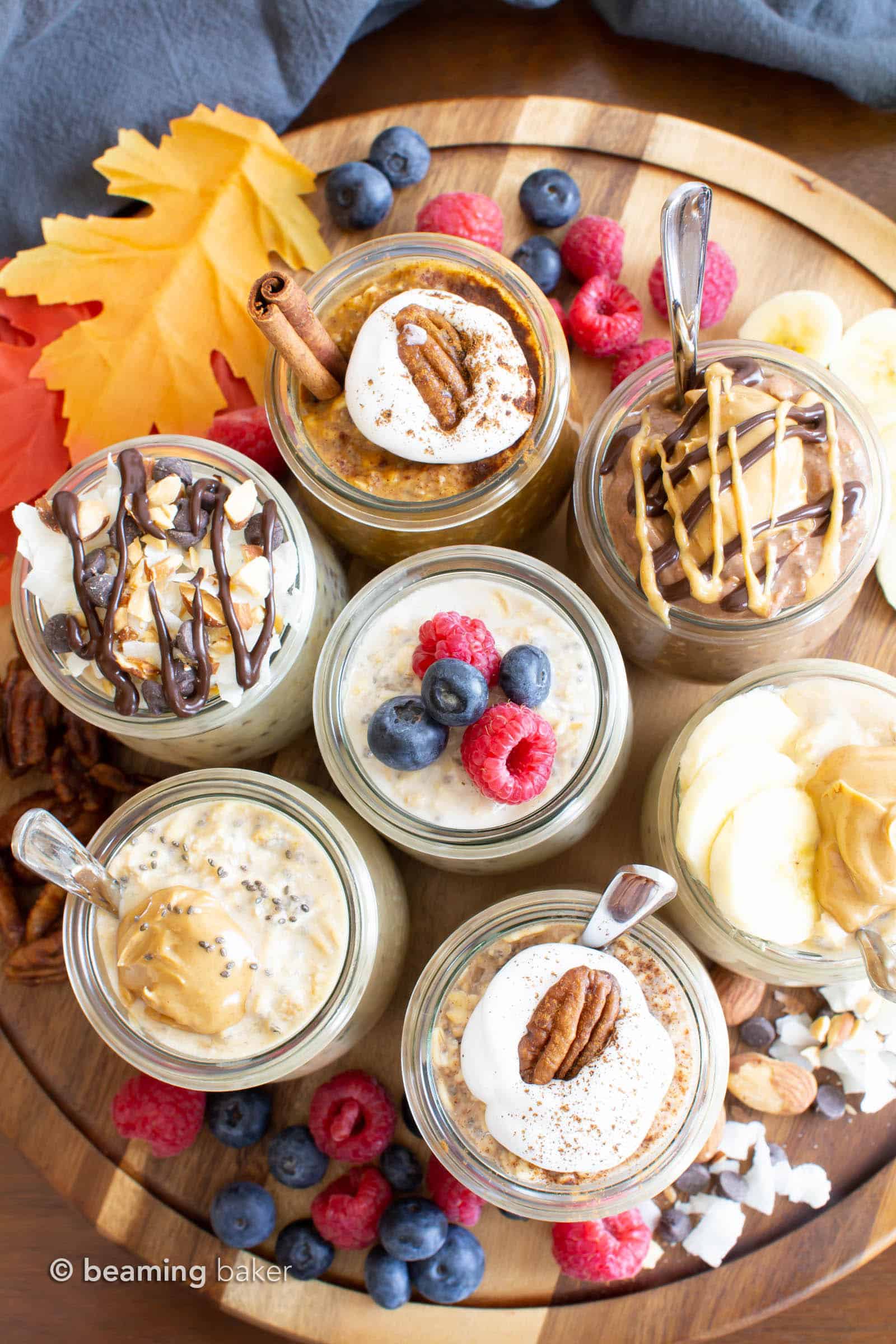 Overhead shot of seven kinds of vegan overnight oats on a wooden tray with berries and assorted nut toppings.