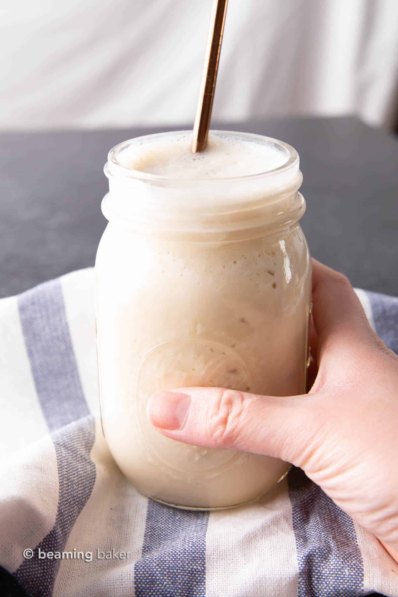 Hand holding protein shake in mason jar with straw in it