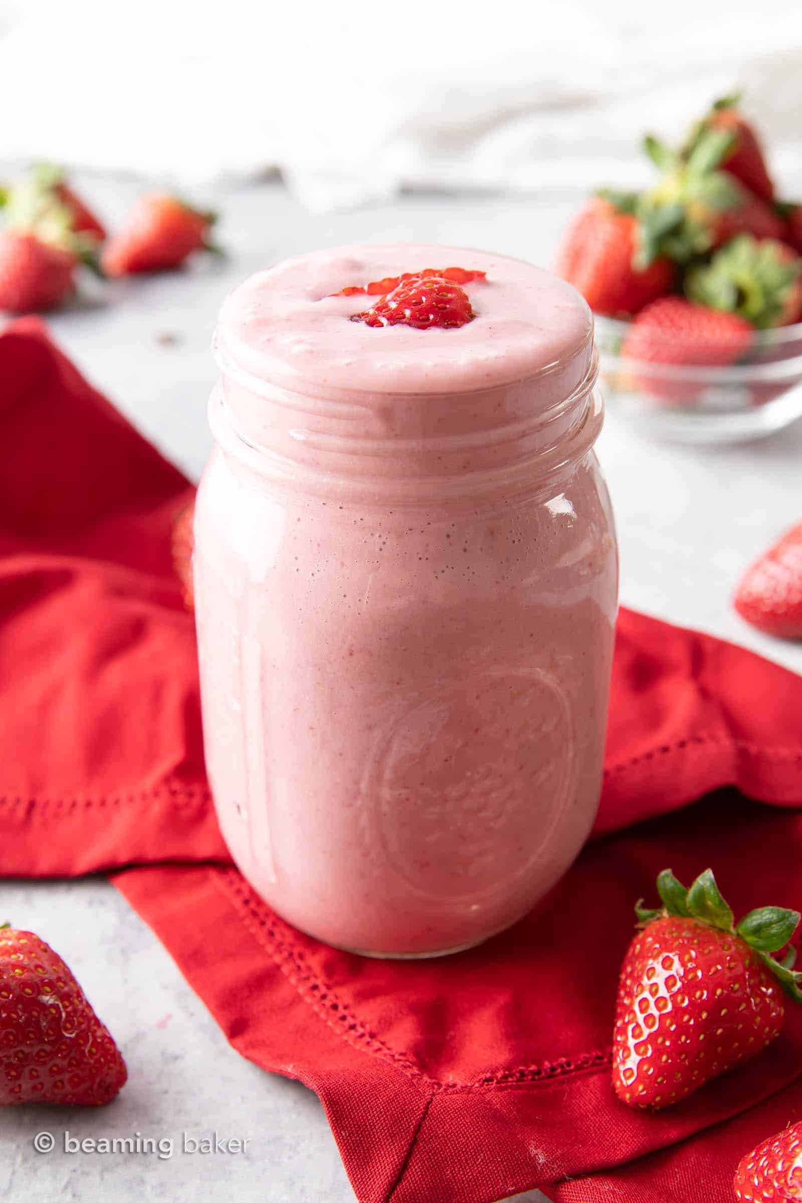mason jar filled with strawberry protein shake on a red napkin, with strawberry slices on top.