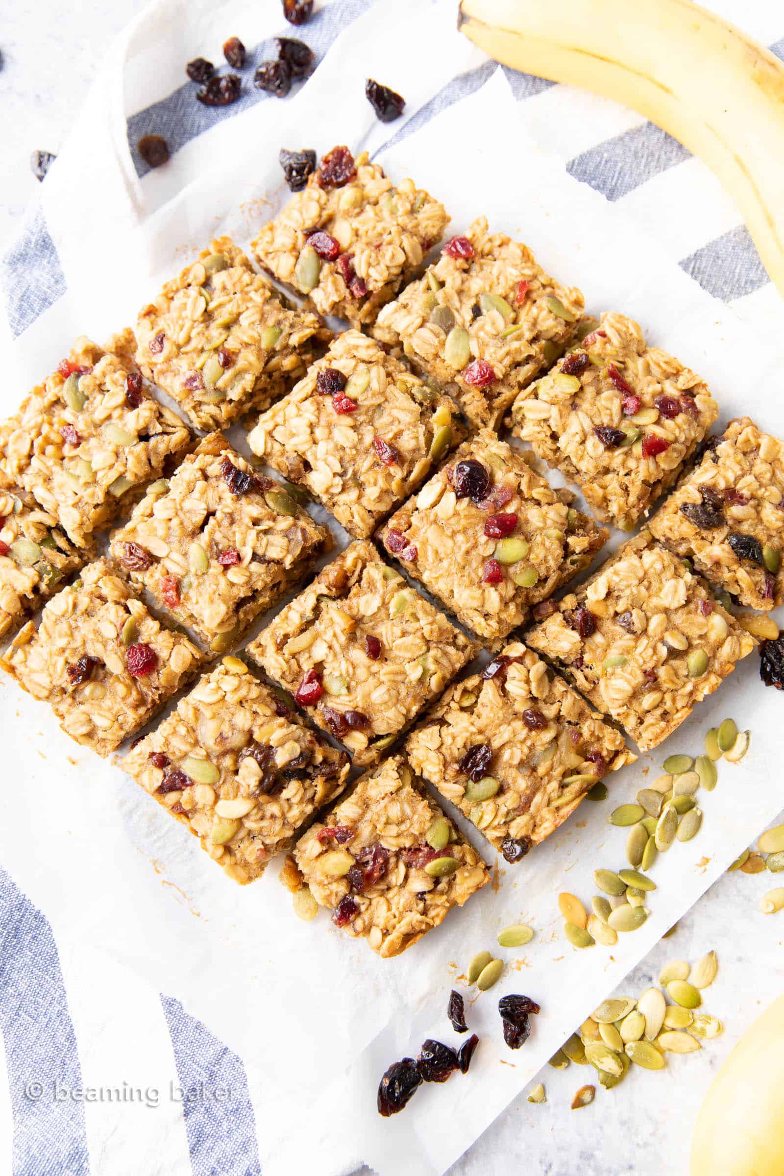 Overhead view of sliced breakfast bars on white parchment paper with seeds and fruit.