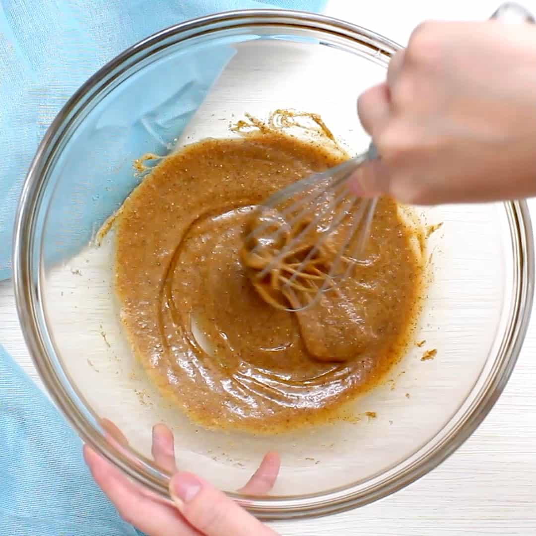 hand whisking almond butter and maple syrup in a glass bowl