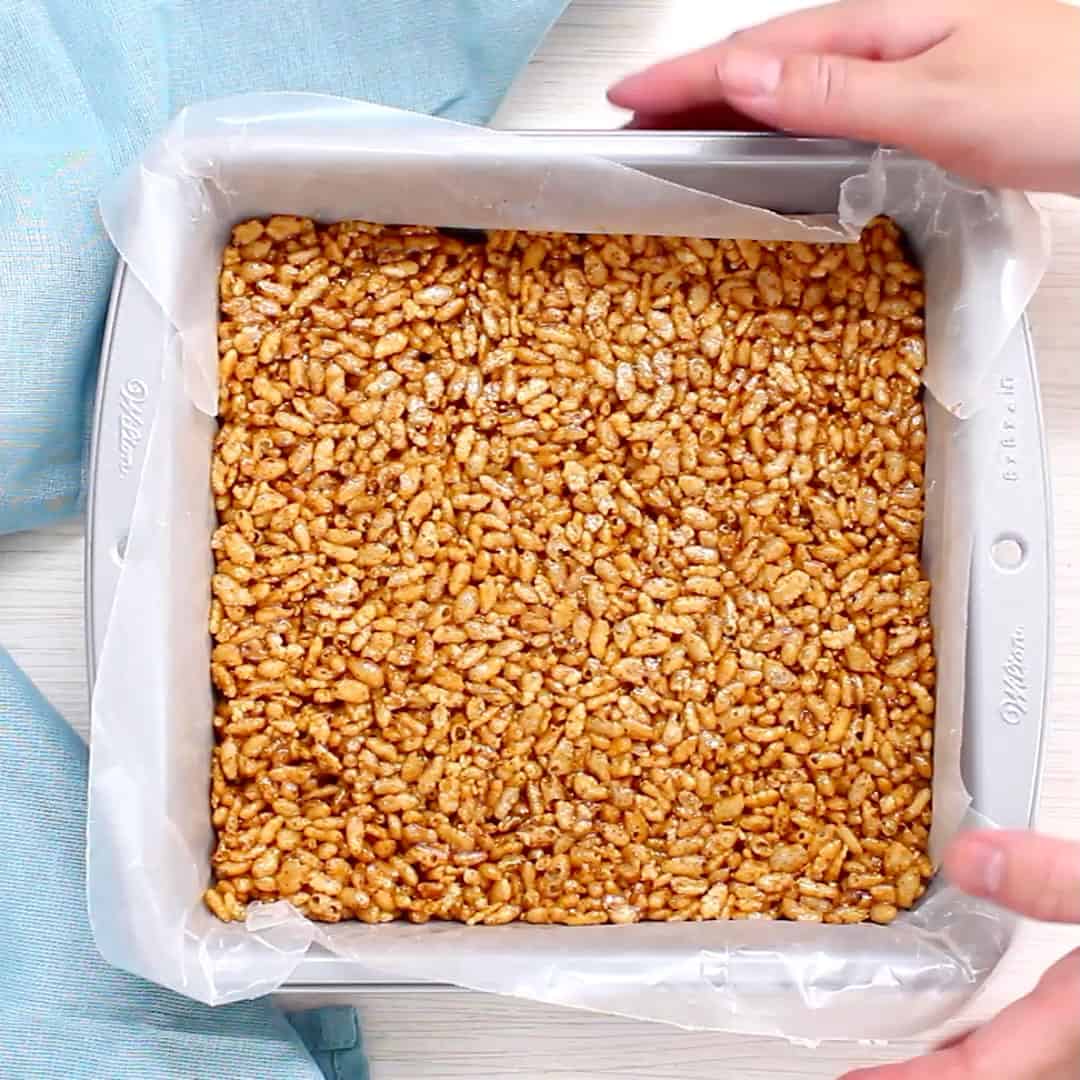 two hands holding a baking pan filled with smoothed and tightly packed rice crispy treats