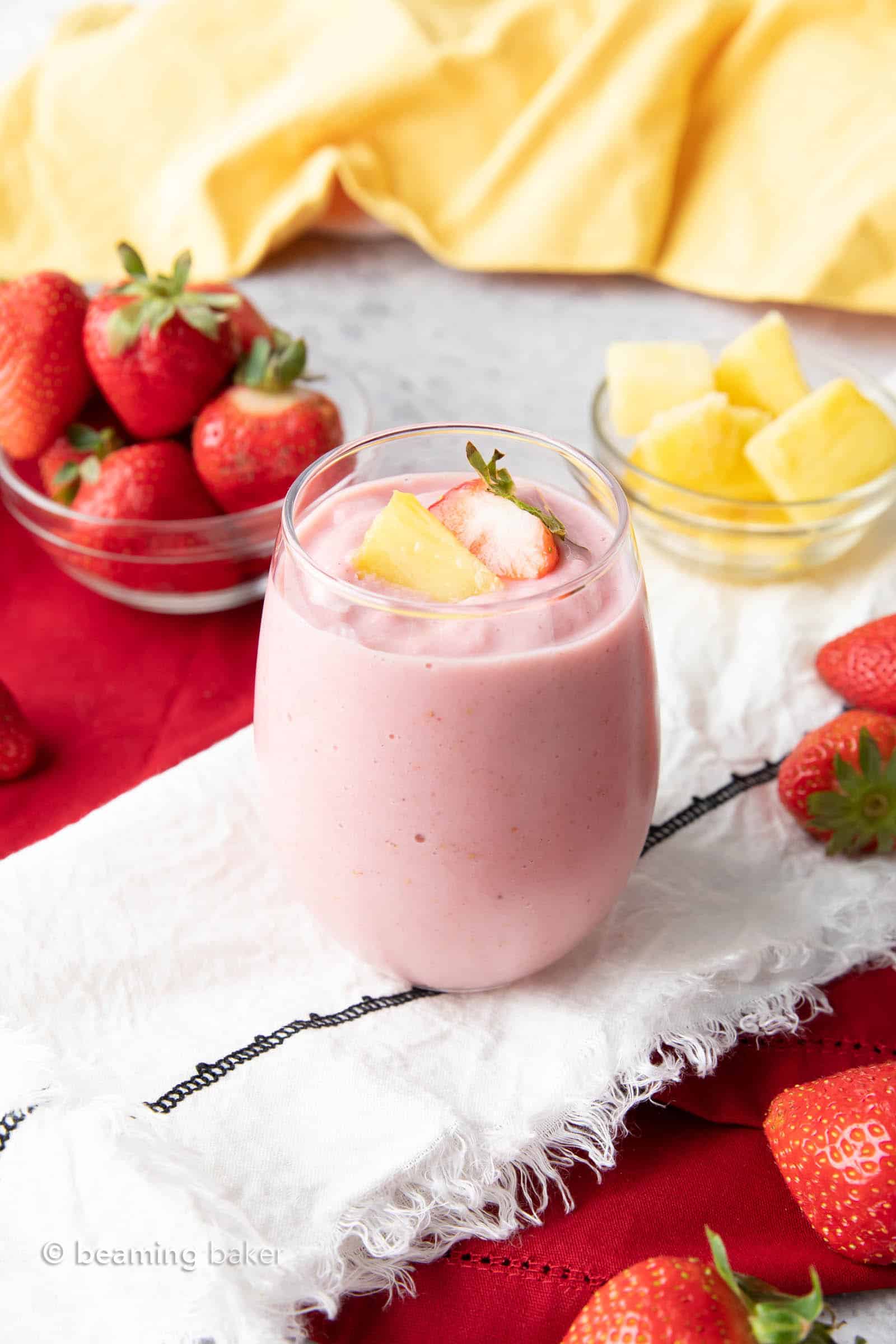 A glass filled with Strawberry Pineapple Smoothie served with fresh strawberries and pineapple chunks