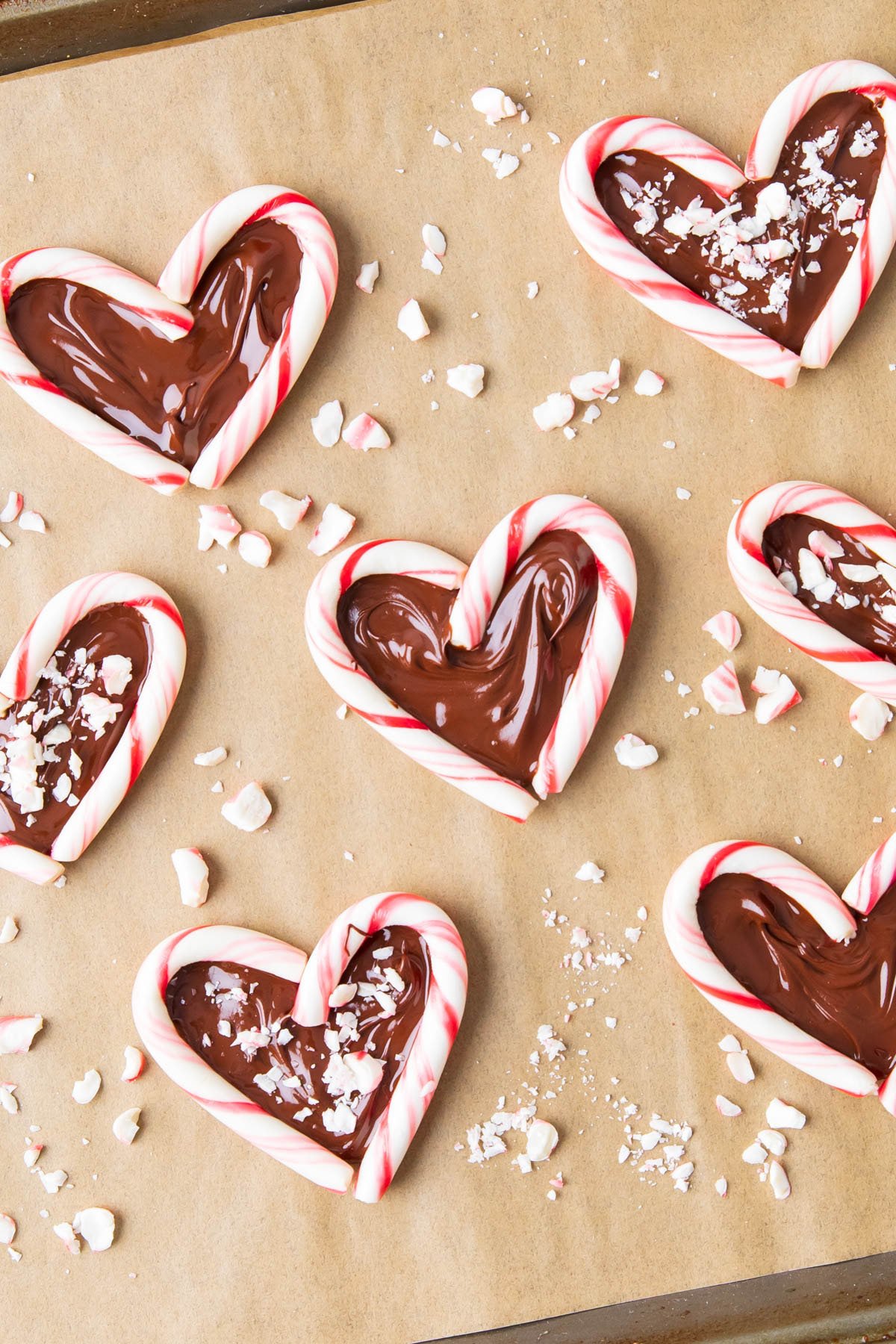 close up of candy cane hearts with chocolate melted into the centers on a parchment paper-lined baking sheet.