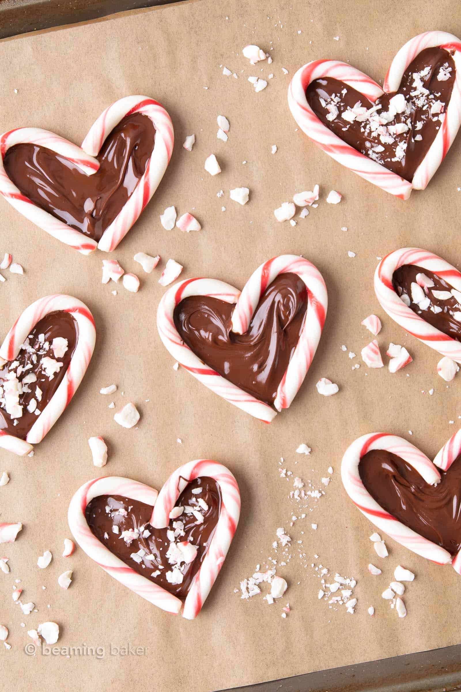 Candy cane hearts being assembled on parchment paper with crushed candy cane pieces scattered around