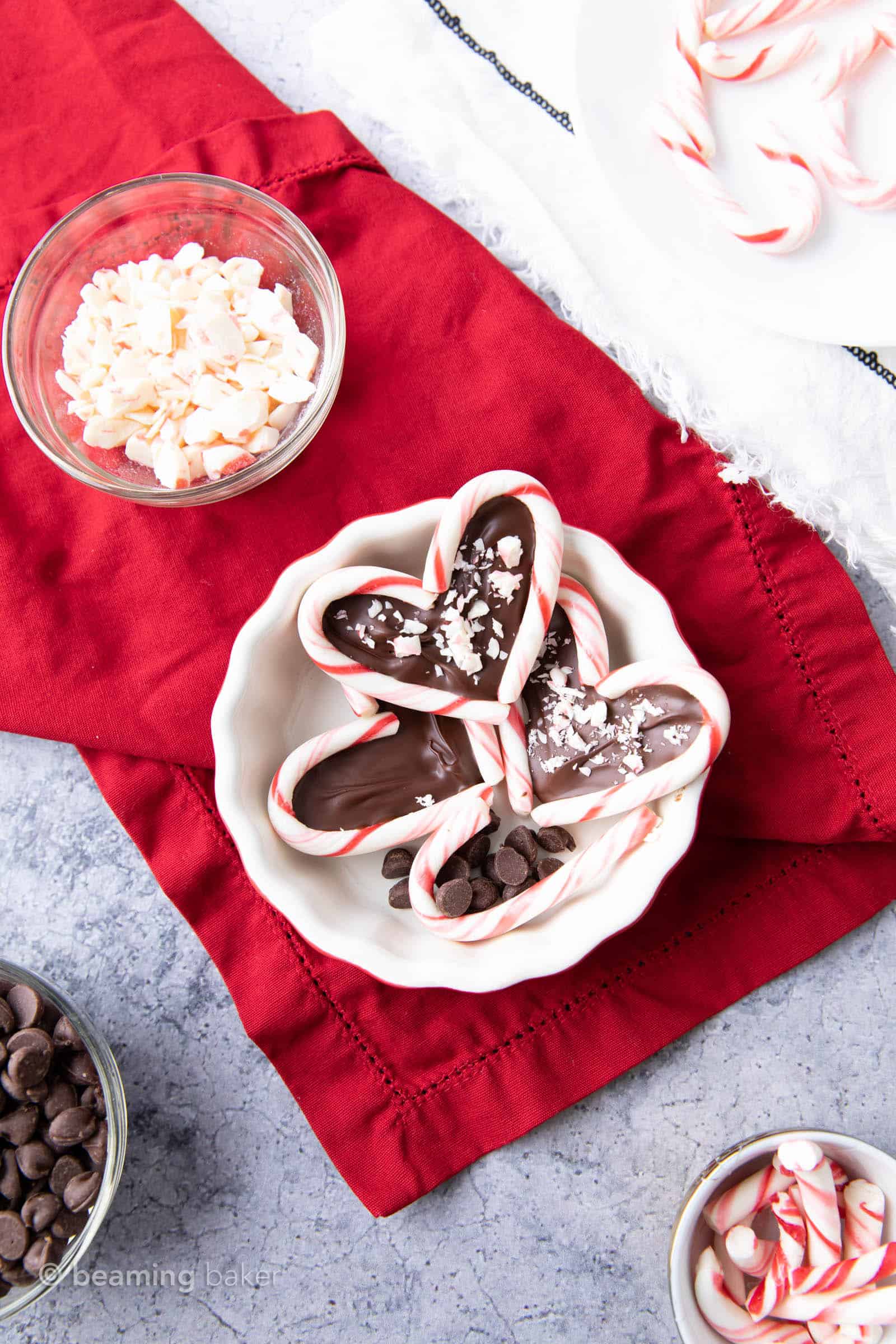 Overhead shot of table with finished candy cane hearts in a bowl, crushed candy canes and chocolate chips in a bowl