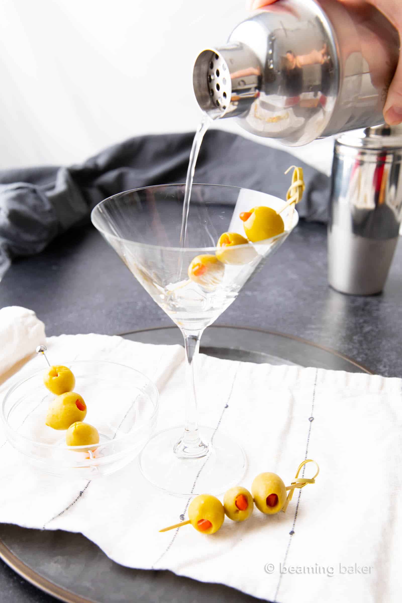 Pouring dirty martini cocktail mixture into a chilled martini glass