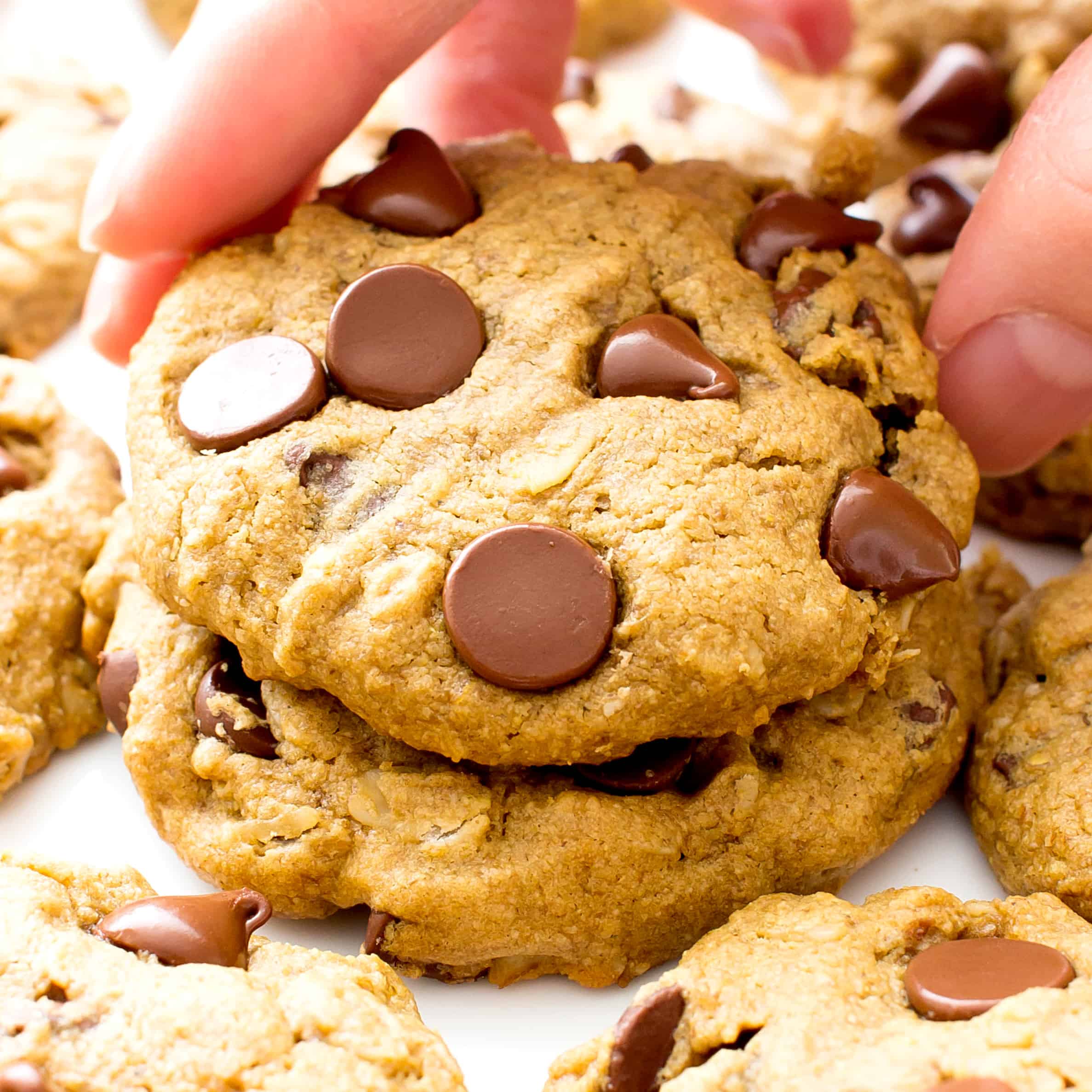 a hand grabbing one soft baked vegan gluten free chocolate chip cookie from a cookie plate