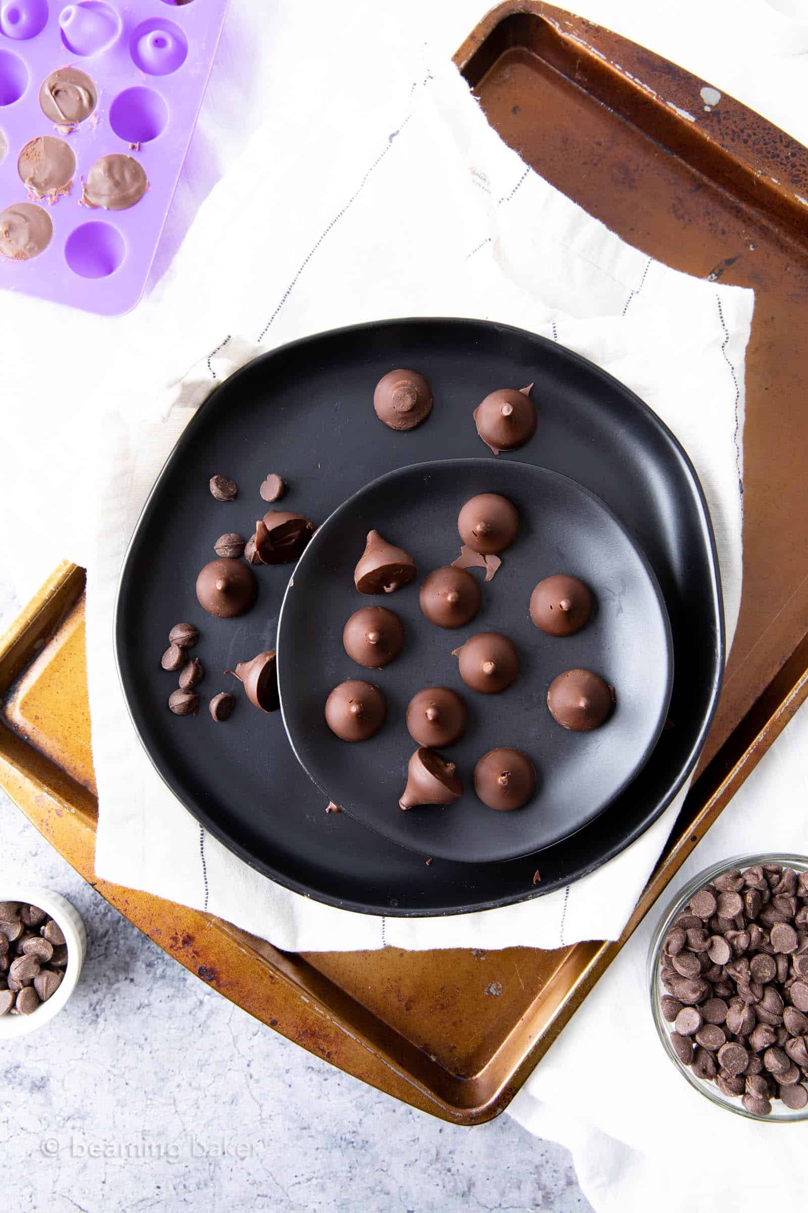 Finished vegan Hershey kisses on serving plate with candy mold, napkins and chocolate in background