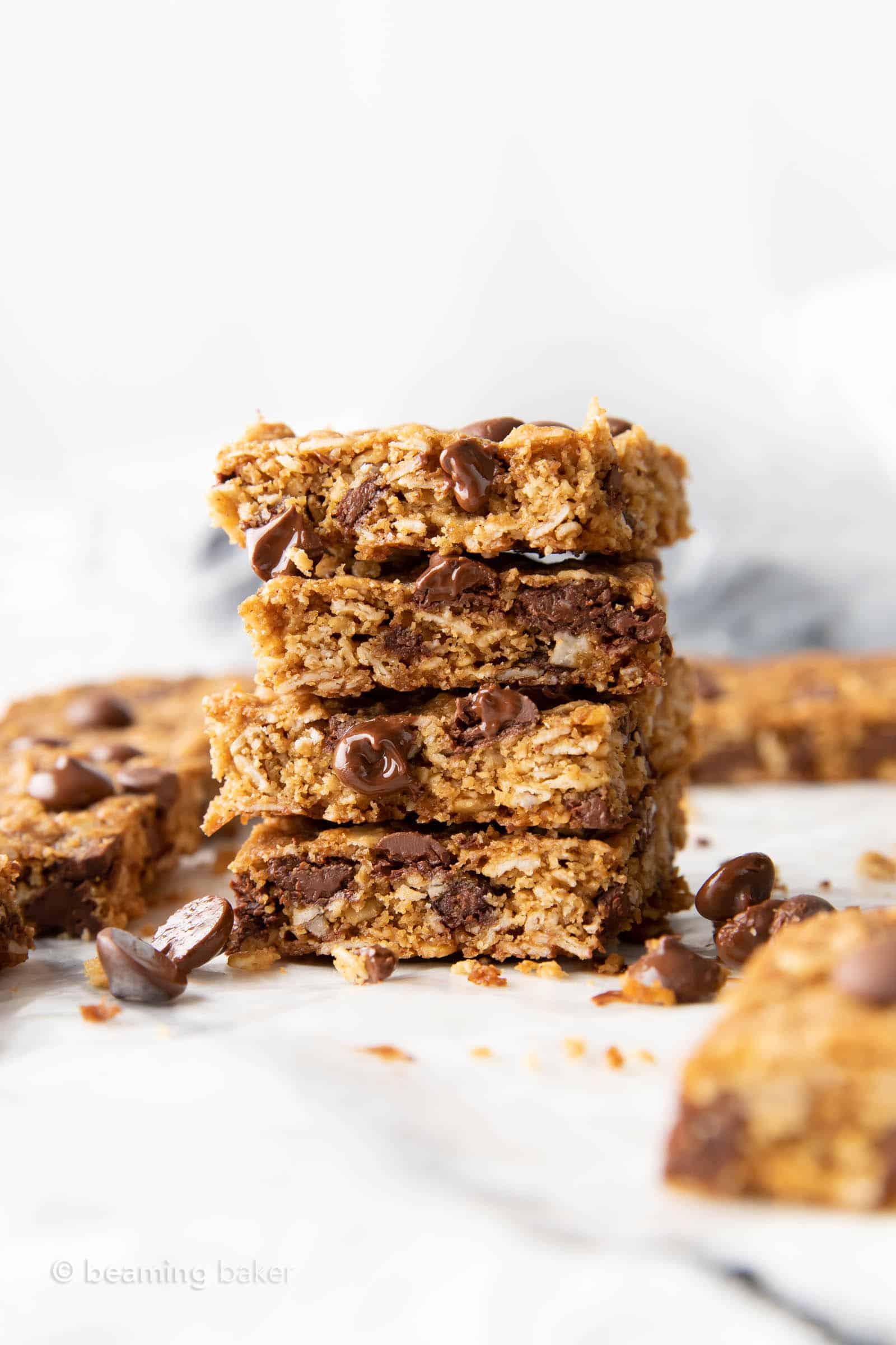 a tall stack of healthy oatmeal cookie bars with melted chocolate chips oozing out and sitting nearby on parchment paper 