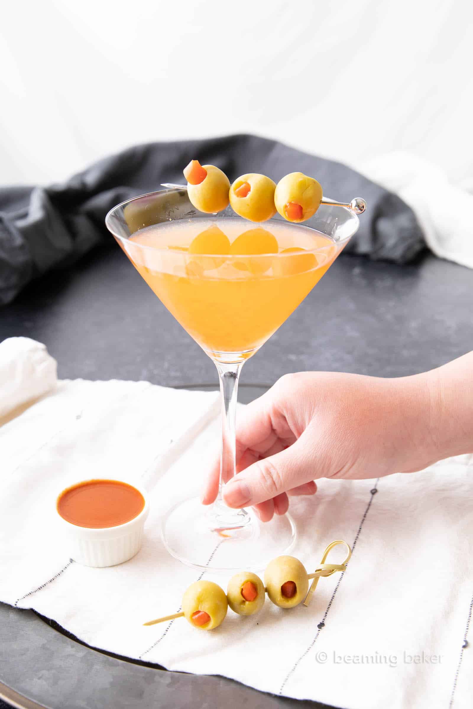 Hand holding hot and dirty martini recipe with hot sauce in foreground