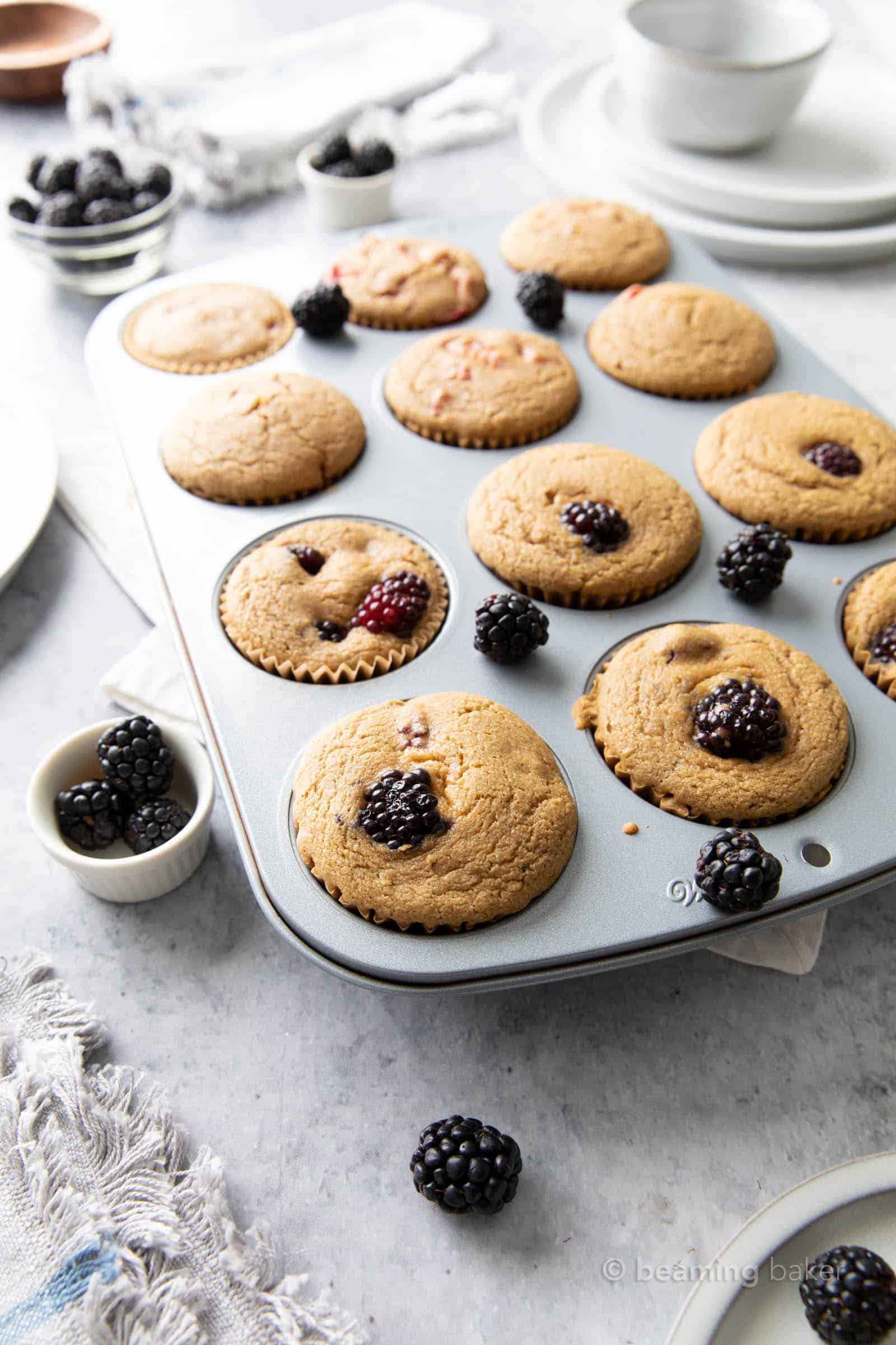 kitchen table with bowls of blueberries and a muffin pan with blackberry muffins in it