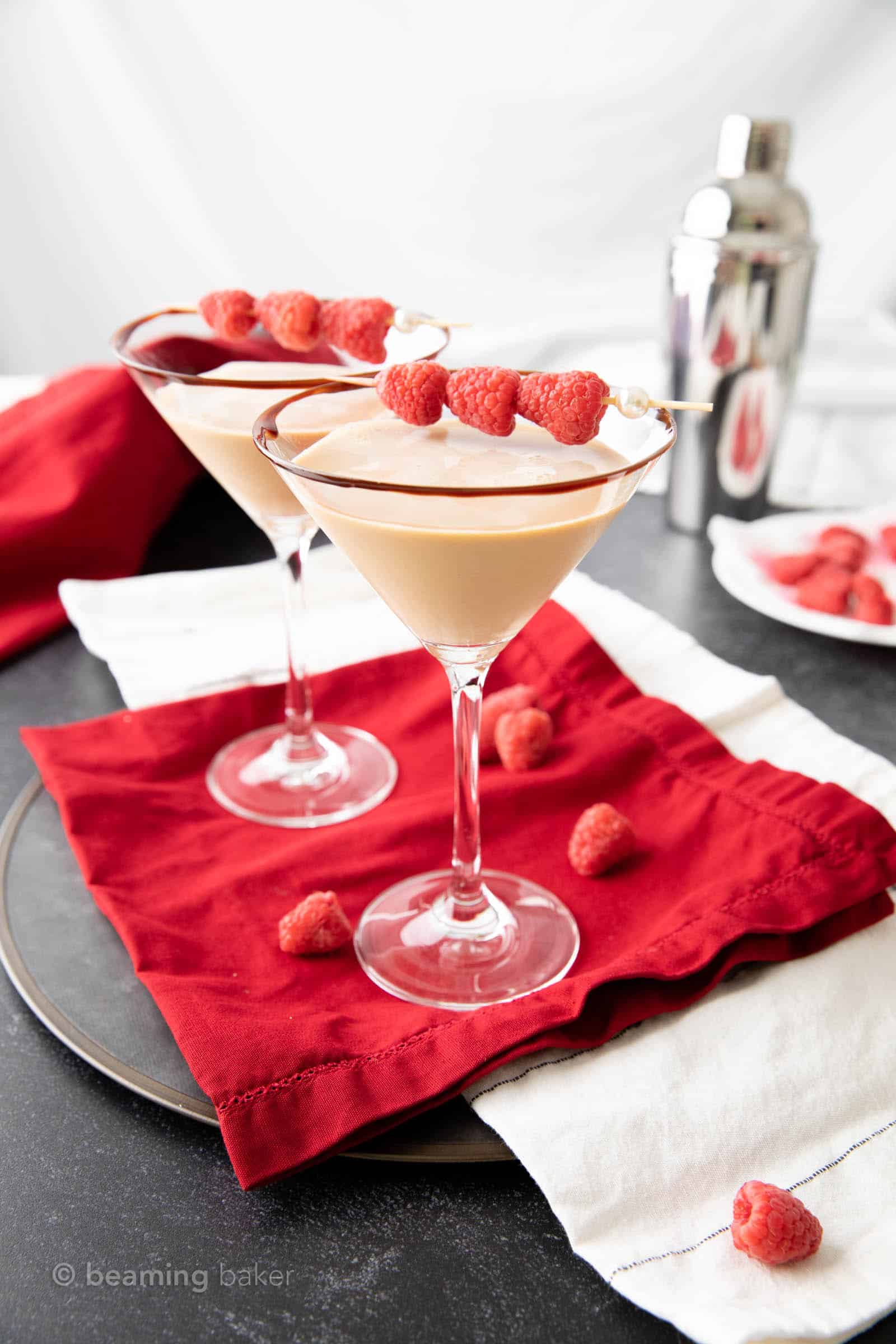 two martini glasses filled with chocolate raspberry martini with a cocktail shaker in the background