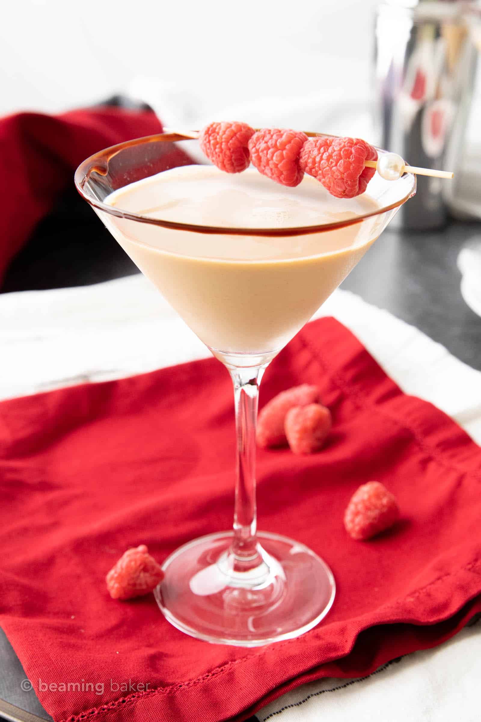 one chocolate raspberry martini in a martini glass rimmed with chocolate syrup and garnished with a raspberry skewer