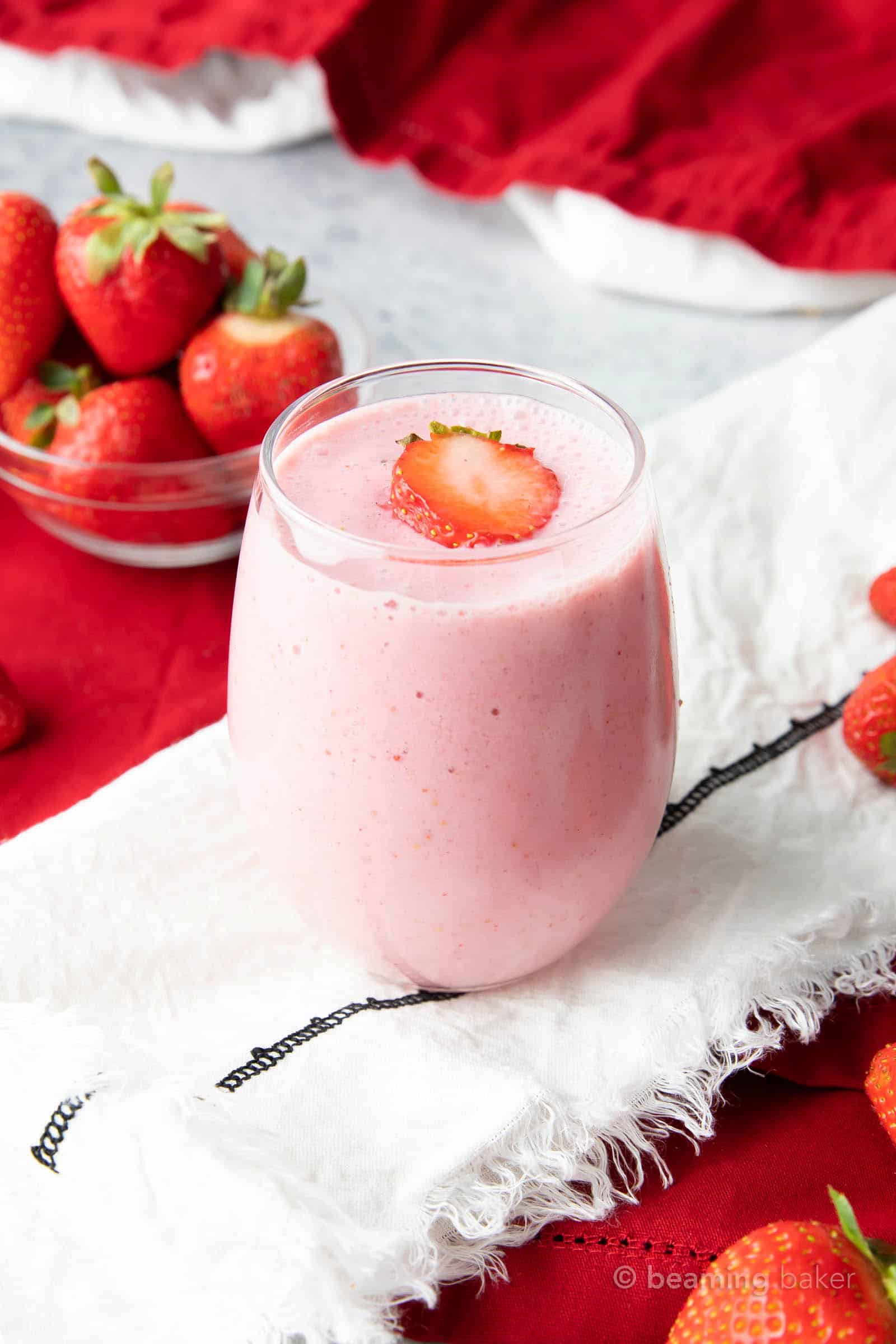 A strawberry smoothie with oat milk on a white napkin with fresh strawberries