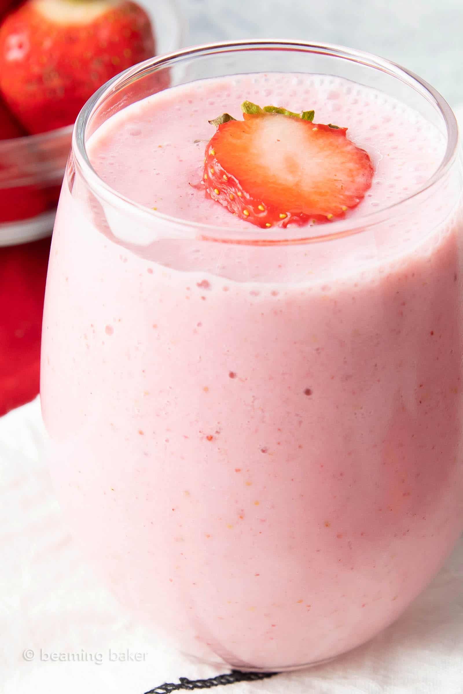 Very closeup shot of oat milk strawberry smoothie in a glass topped with a strawberry slice