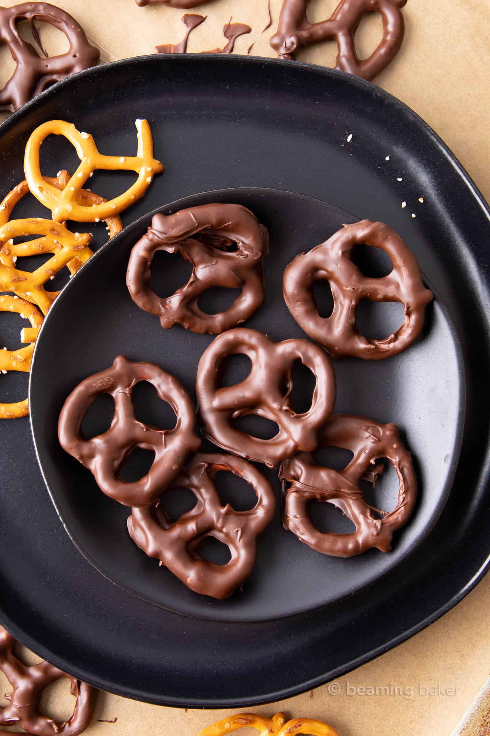 Vegan chocolate covered pretzels on a black plate with more pretzels