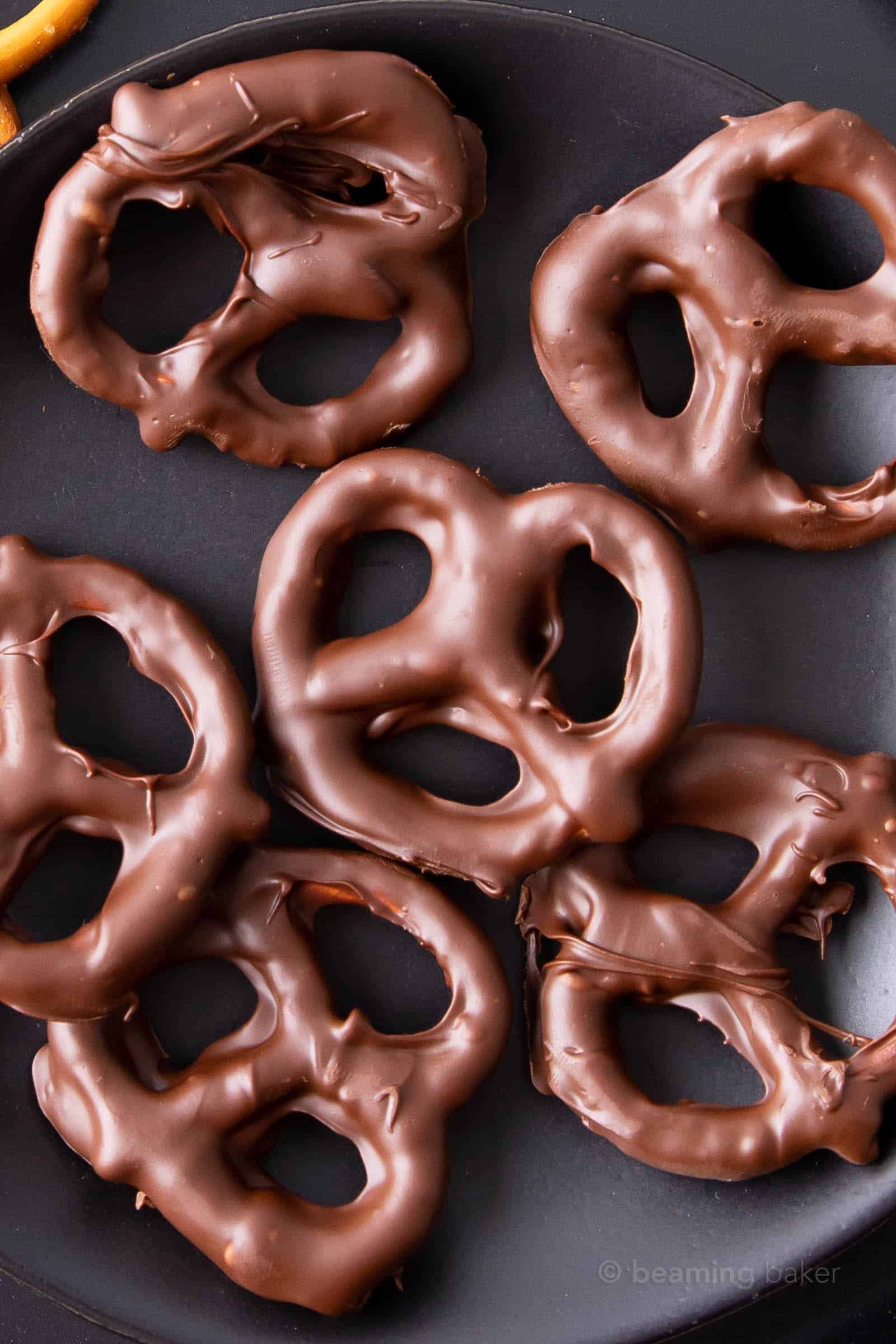 Closeup of vegan chocolate covered pretzels on a black plate with one uncovered pretzel showing