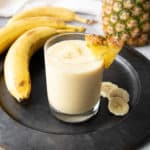 Pineapple Banana Smoothie on a grey plate with ingredients in the background.