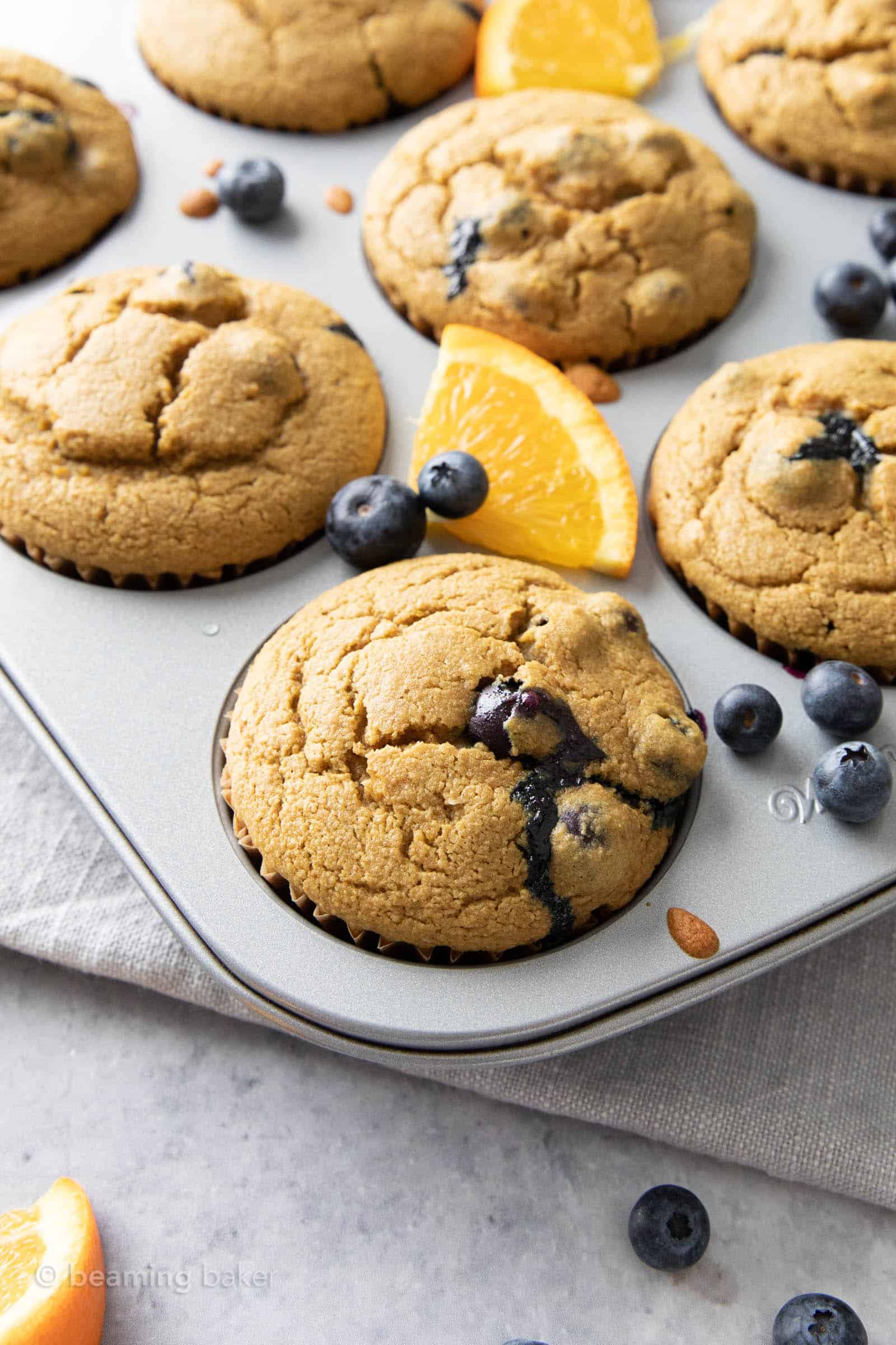 blueberry bursting in the middle of a blueberry orange muffin cooling in baking pan