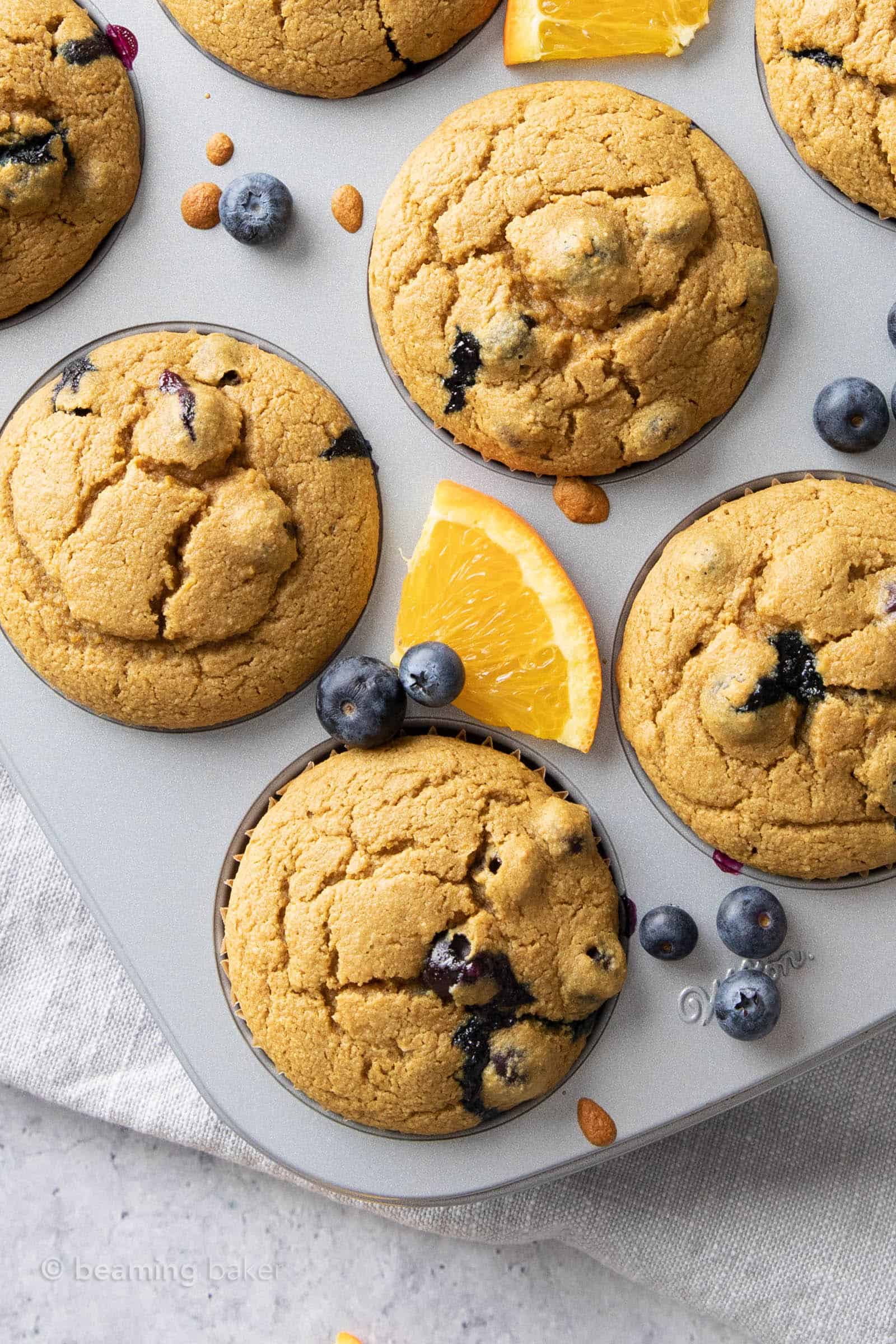 Blueberry orange muffins surrounded by orange slices and fresh blueberries in pan