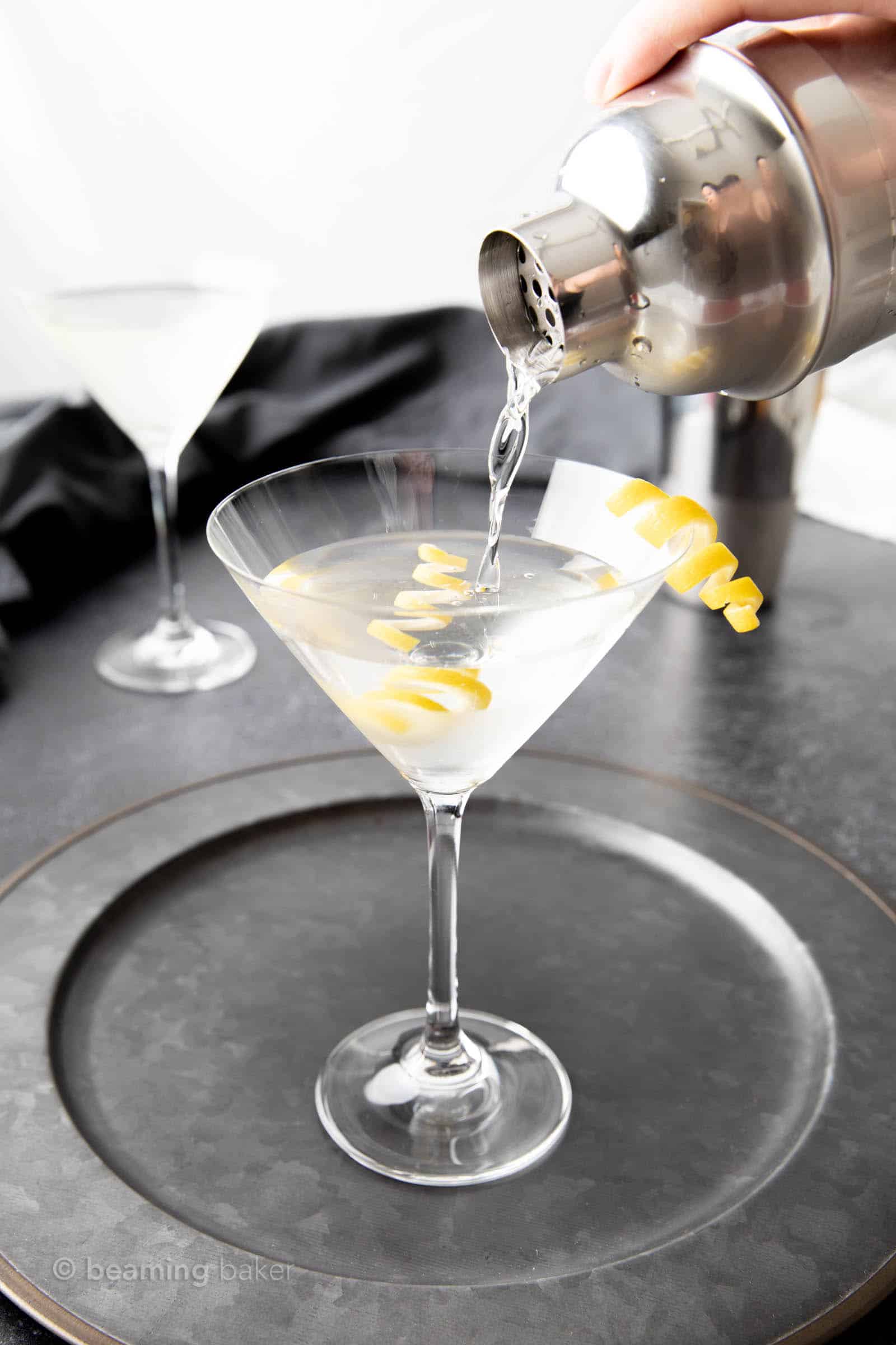Straining classic vodka martini from shaker into garnished martini glass