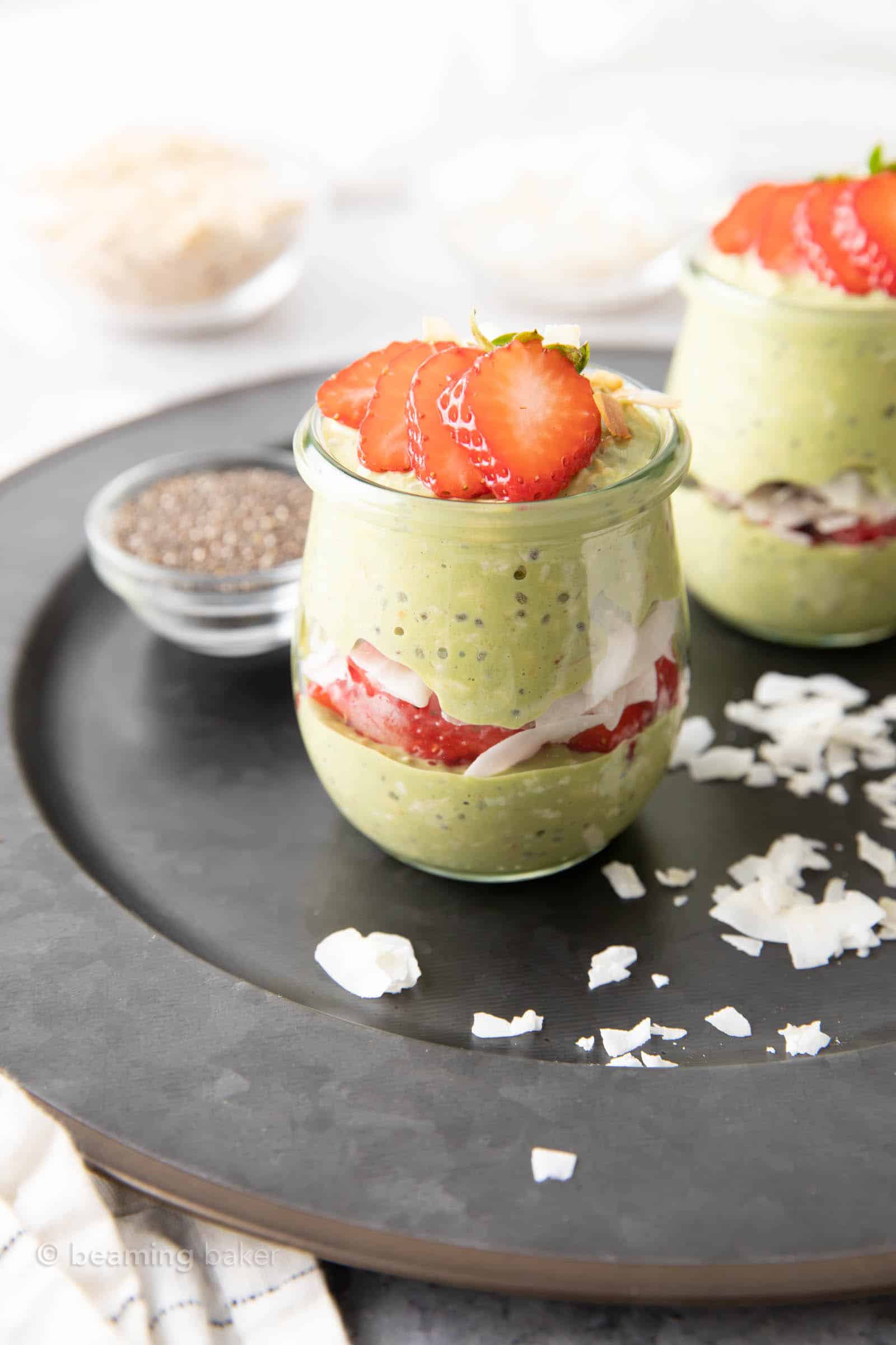 angled photo of matcha overnight oats in two glass jars with a glass of chia seeds and coconut shreds