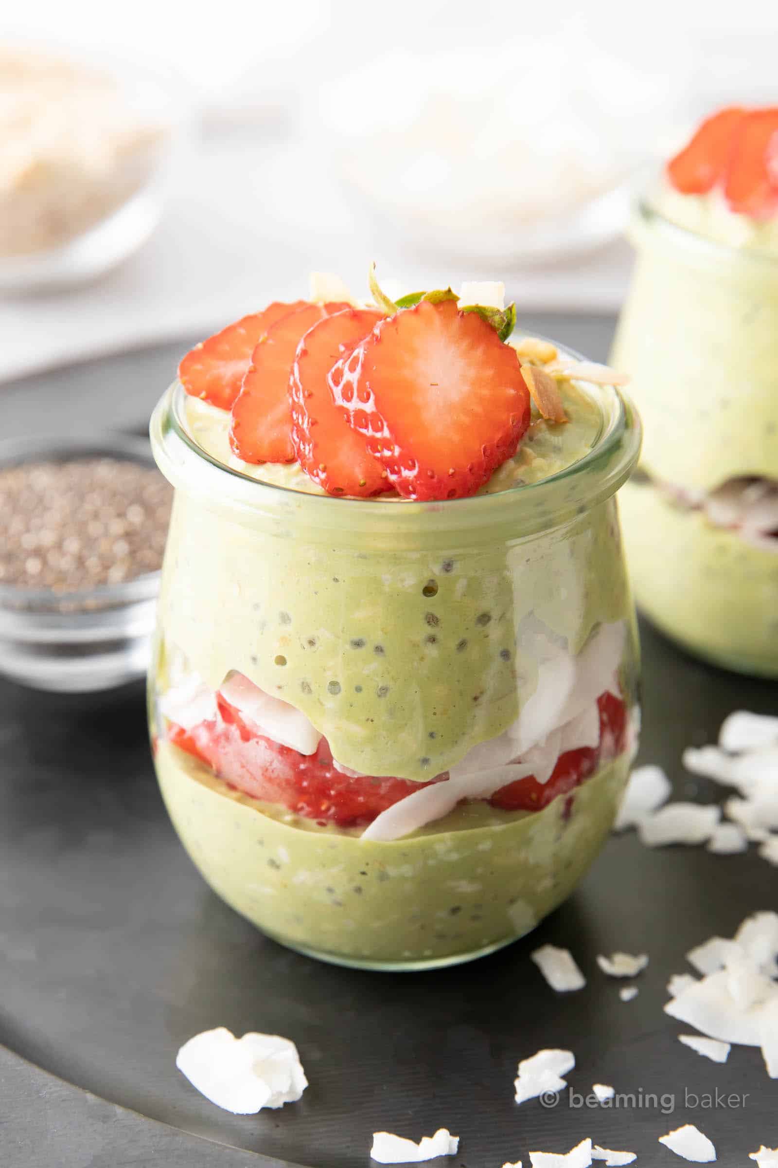 Two jars of matcha overnight oats on a serving platter with overnight oat ingredients on a table