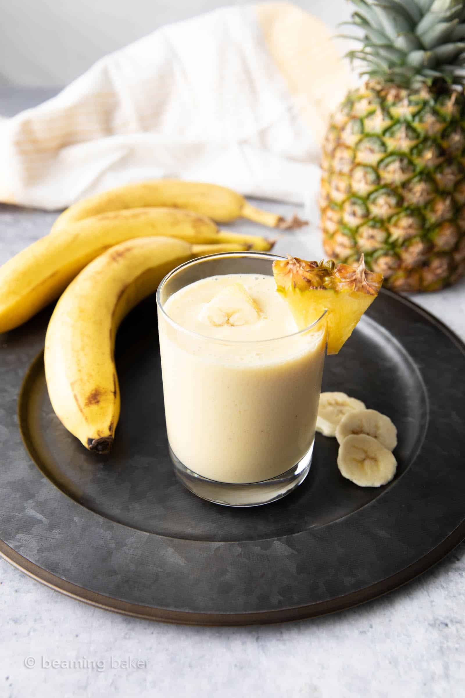 pineapple banana smoothie recipe in a glass with bananas and pineapples on a serving tray