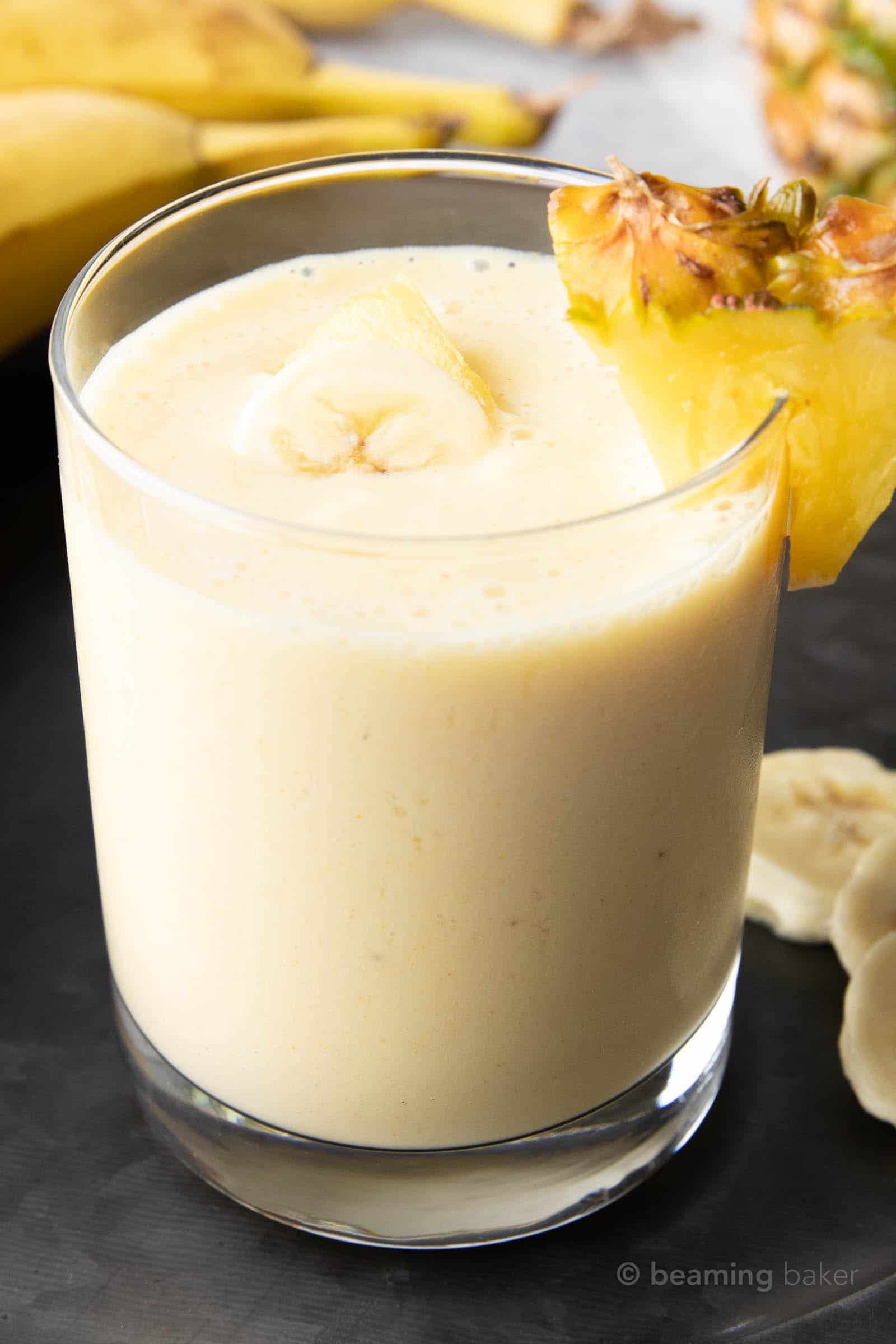 closeup shot of creamy pineapple and banana smoothie with banana slice and pineapple wedge